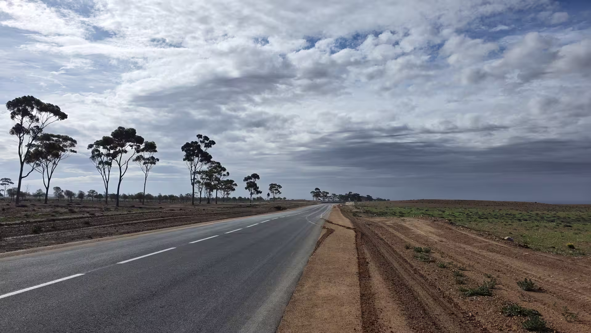 A quiet road stretching through open countryside south of Oujda beneath dramatic clouds.