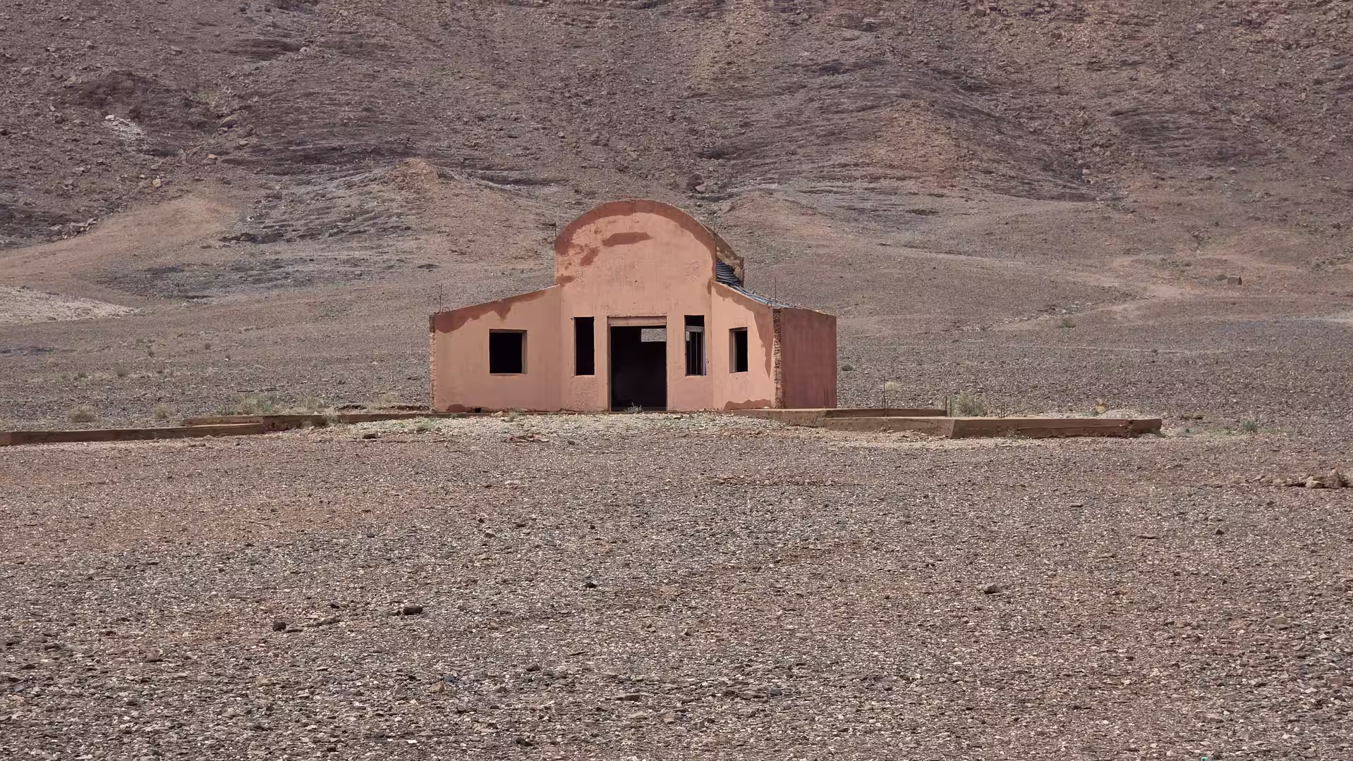 A small pink building standing alone in a rocky desert landscape in eastern Morocco.