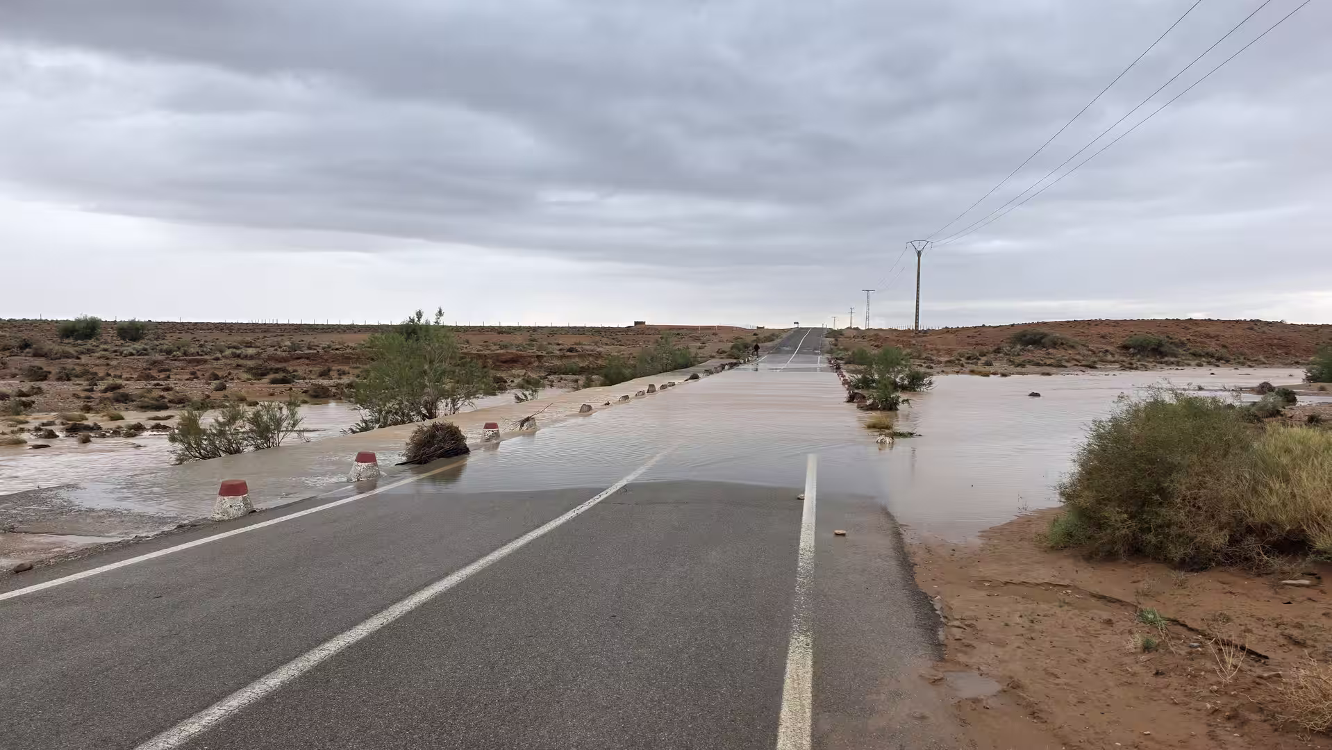 Floodwater flowing across a desert road in eastern Morocco beneath dark storm clouds.