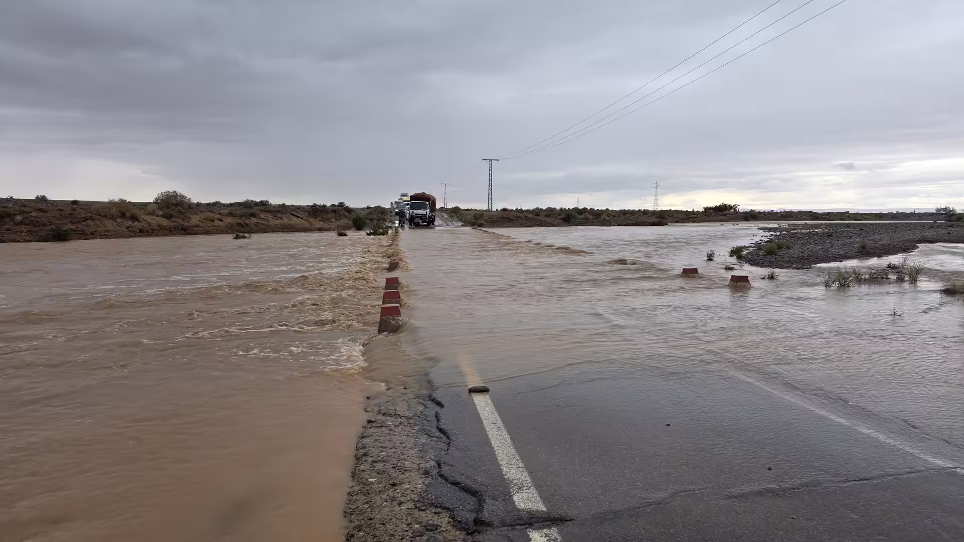 Trucks stopped at a flooded desert road crossing in eastern Morocco after heavy rainfall.