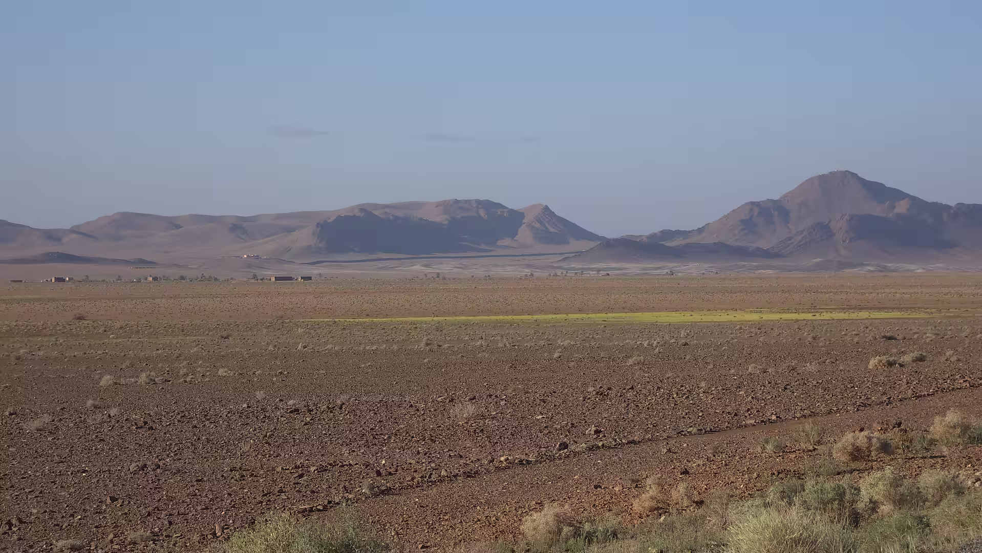 Wide rocky plain leading toward isolated mountains in eastern Morocco under clear morning light.
