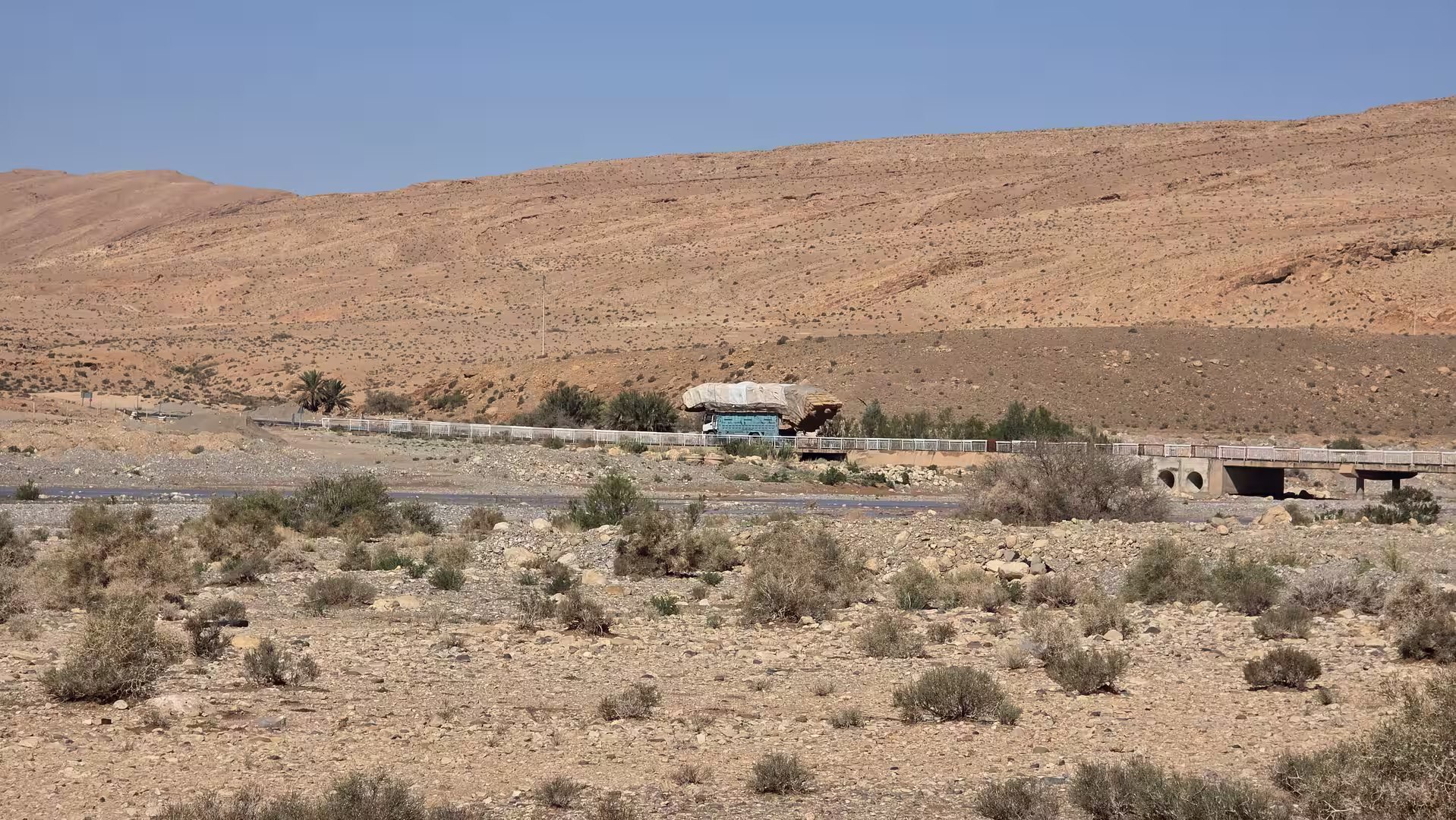 Small bridge crossing a dry desert valley with sparse vegetation and rocky hills near Bouanane, Morocco.