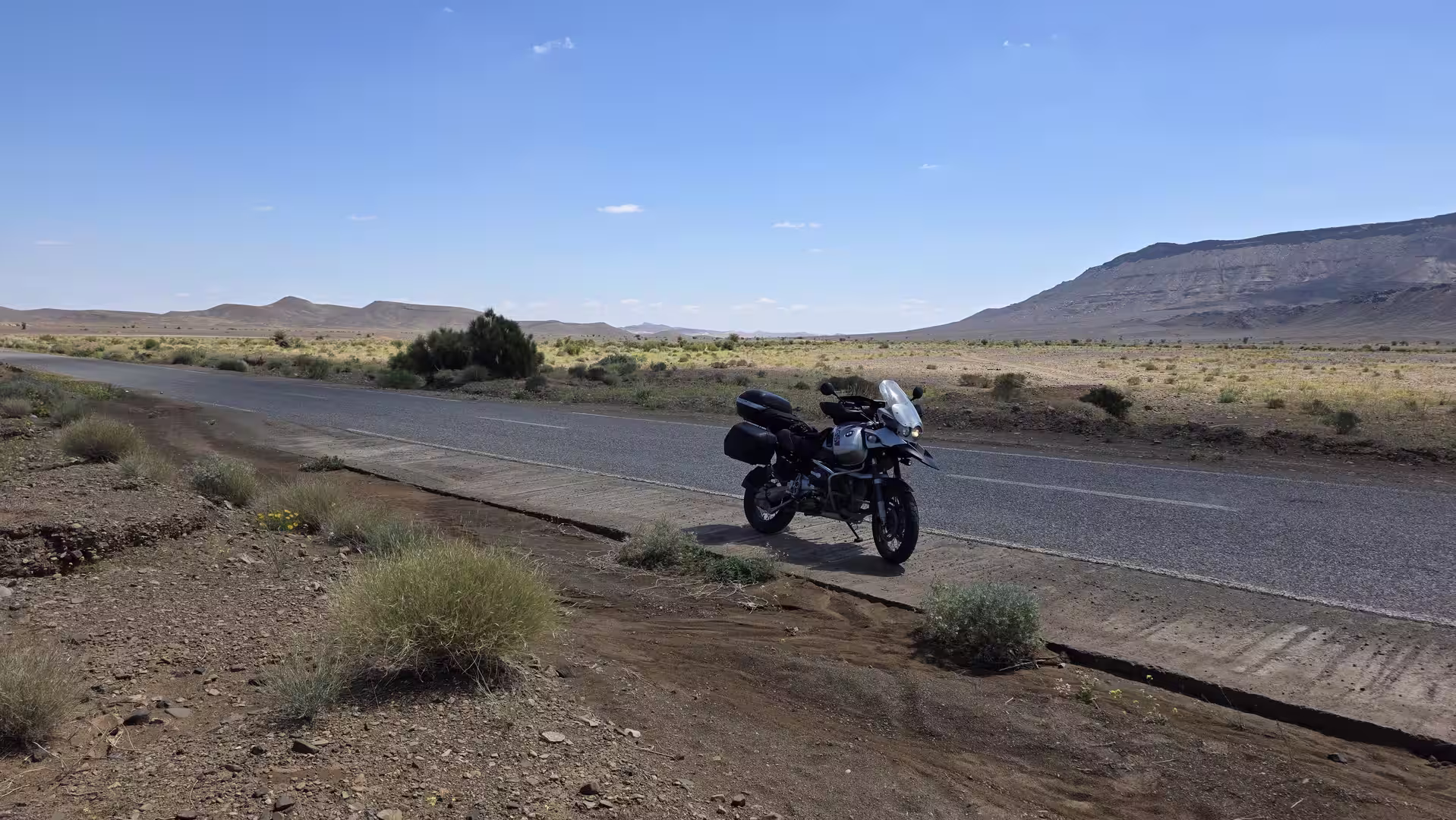 Adventure motorcycle parked beside a remote road in a semi arid landscape with low mountains and open desert plains in eastern Morocco.
