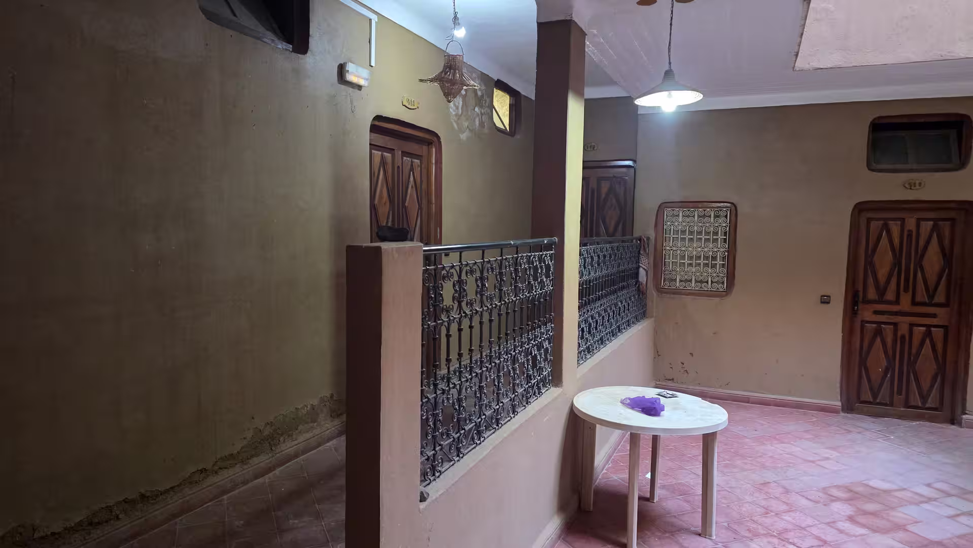 Interior corridor with traditional wooden doors, decorative railings, and warm lighting inside Hotel La Rose des Sables in Zagora.