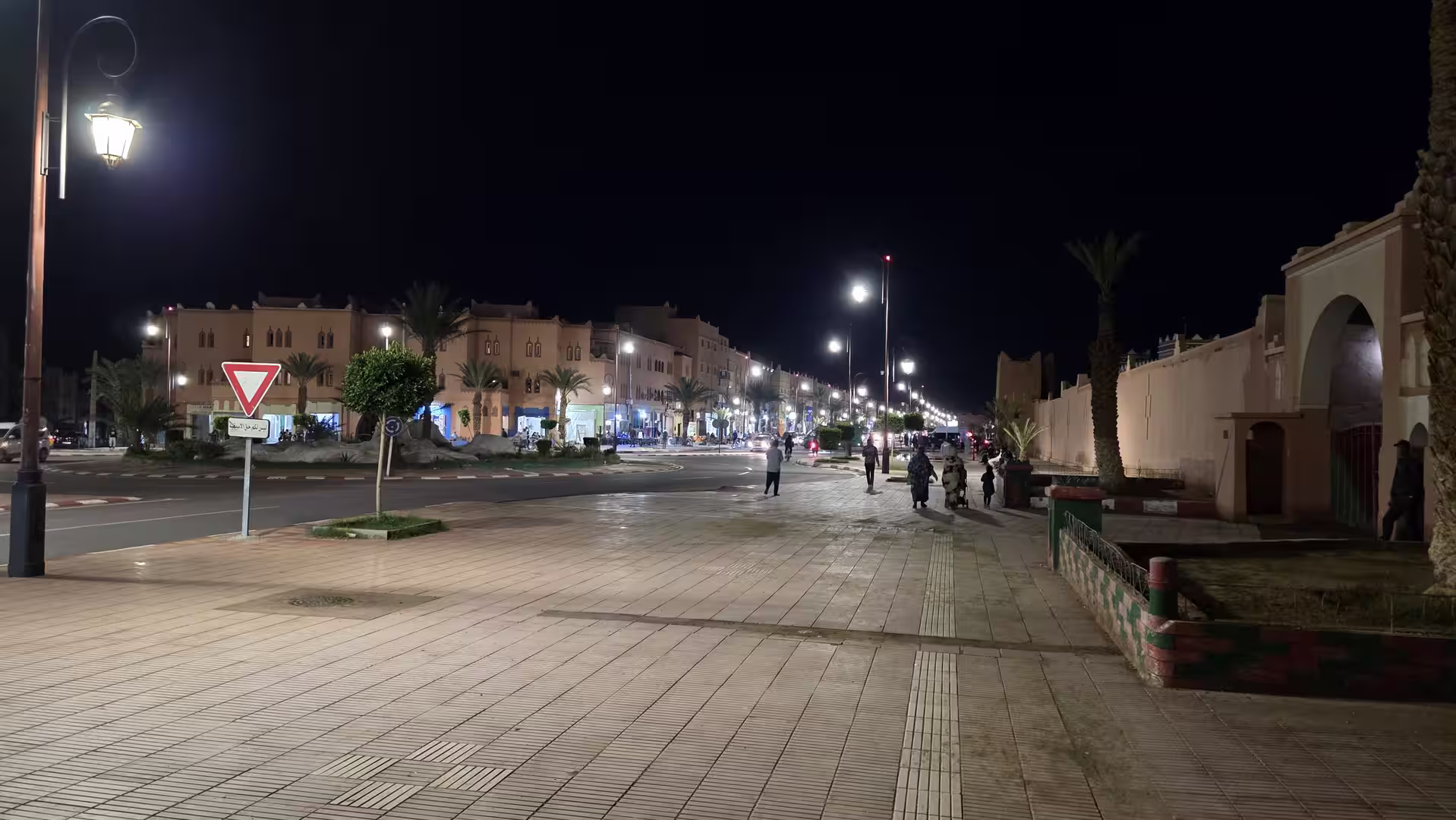 Wide illuminated boulevard in Zagora at night with palm trees, pedestrians, and softly lit buildings.