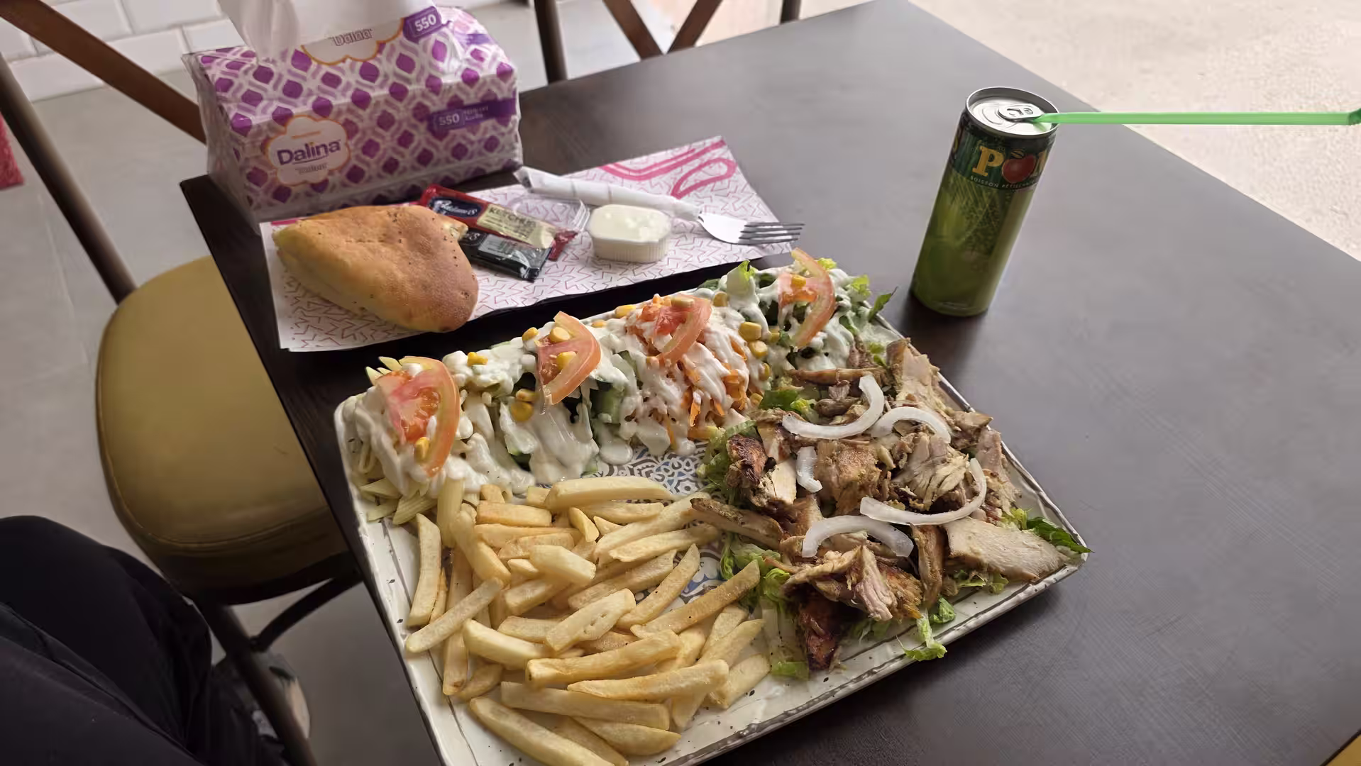 Large meal with grilled meat, fries, mixed salads, bread and a canned soft drink served on a dark table.