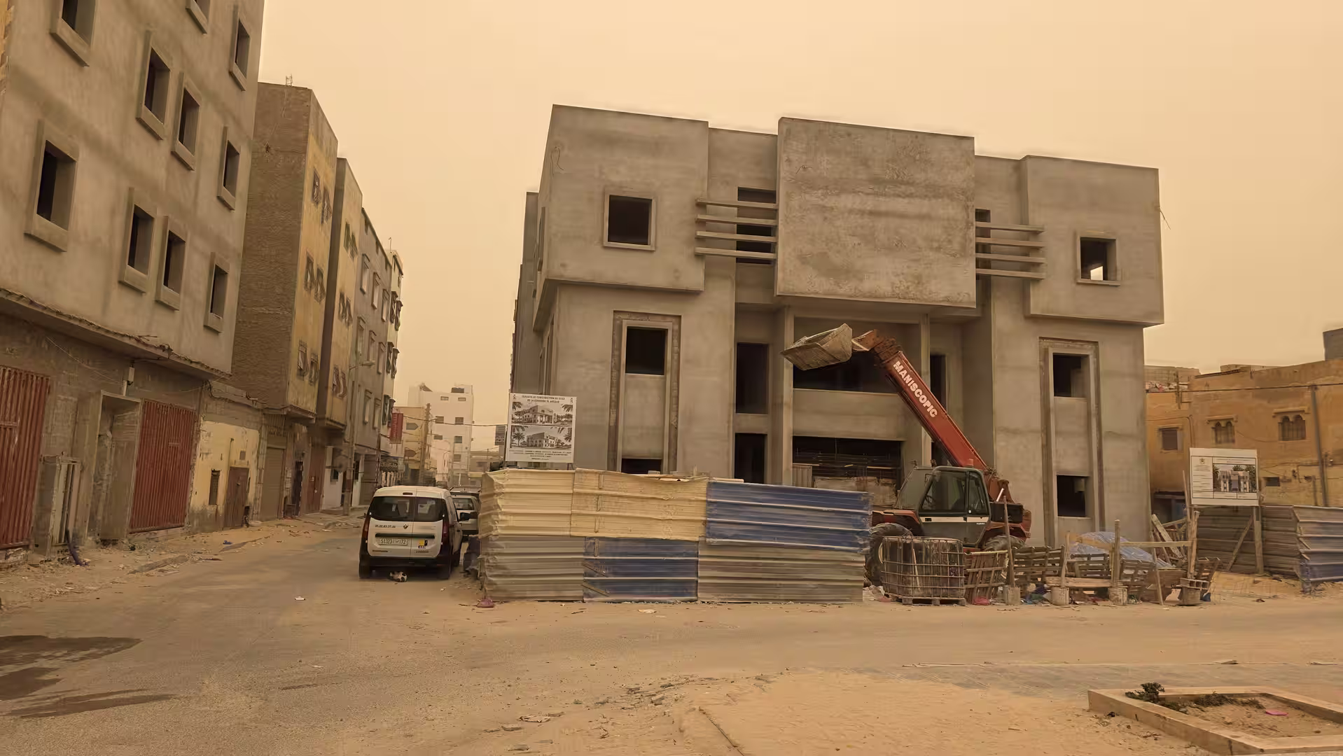 Contemporary concrete building under construction in a dusty urban street with orange haze over Dakhla.