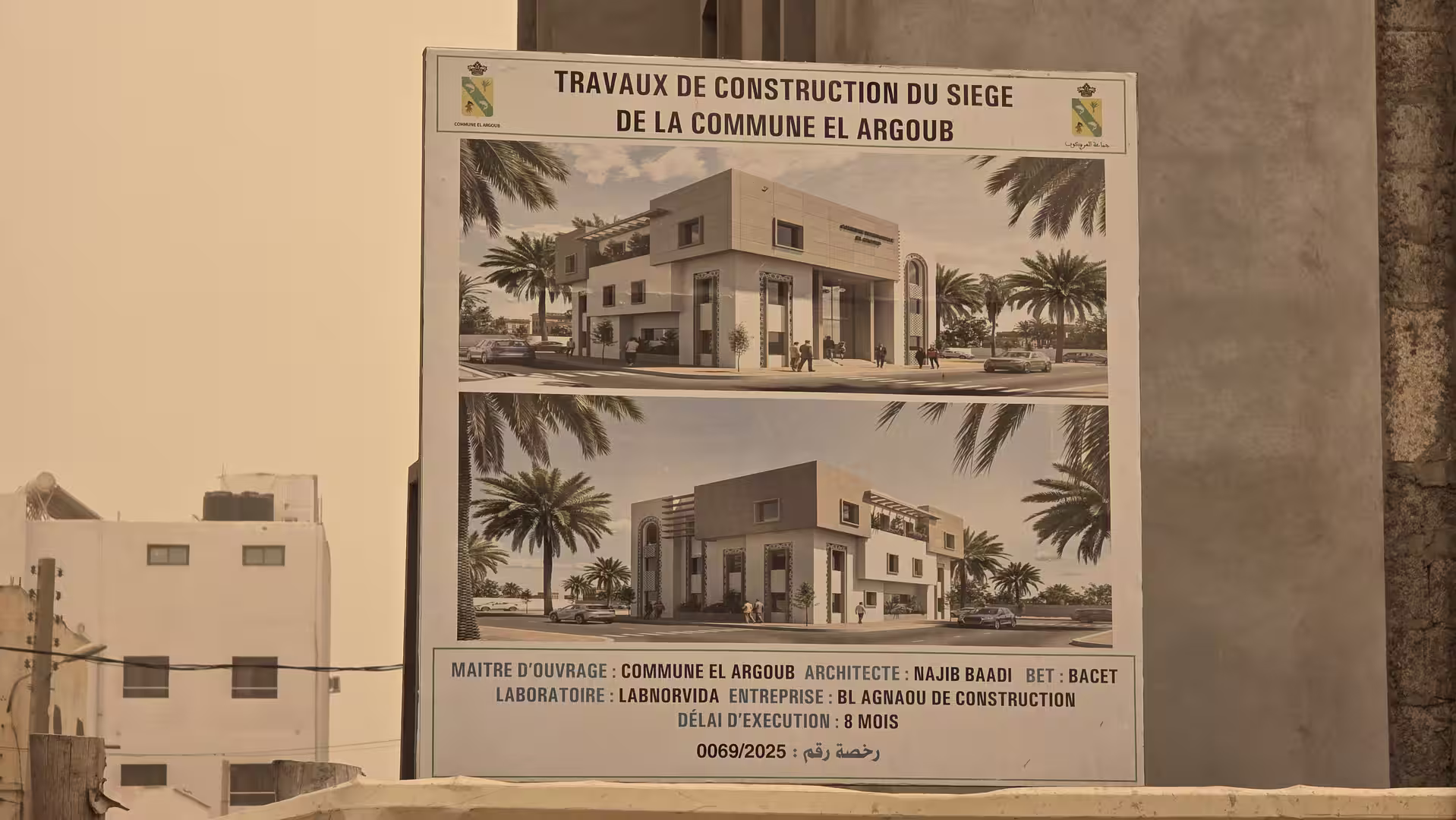 Project signboard showing architectural renderings of the future El Argoub municipal building during construction.