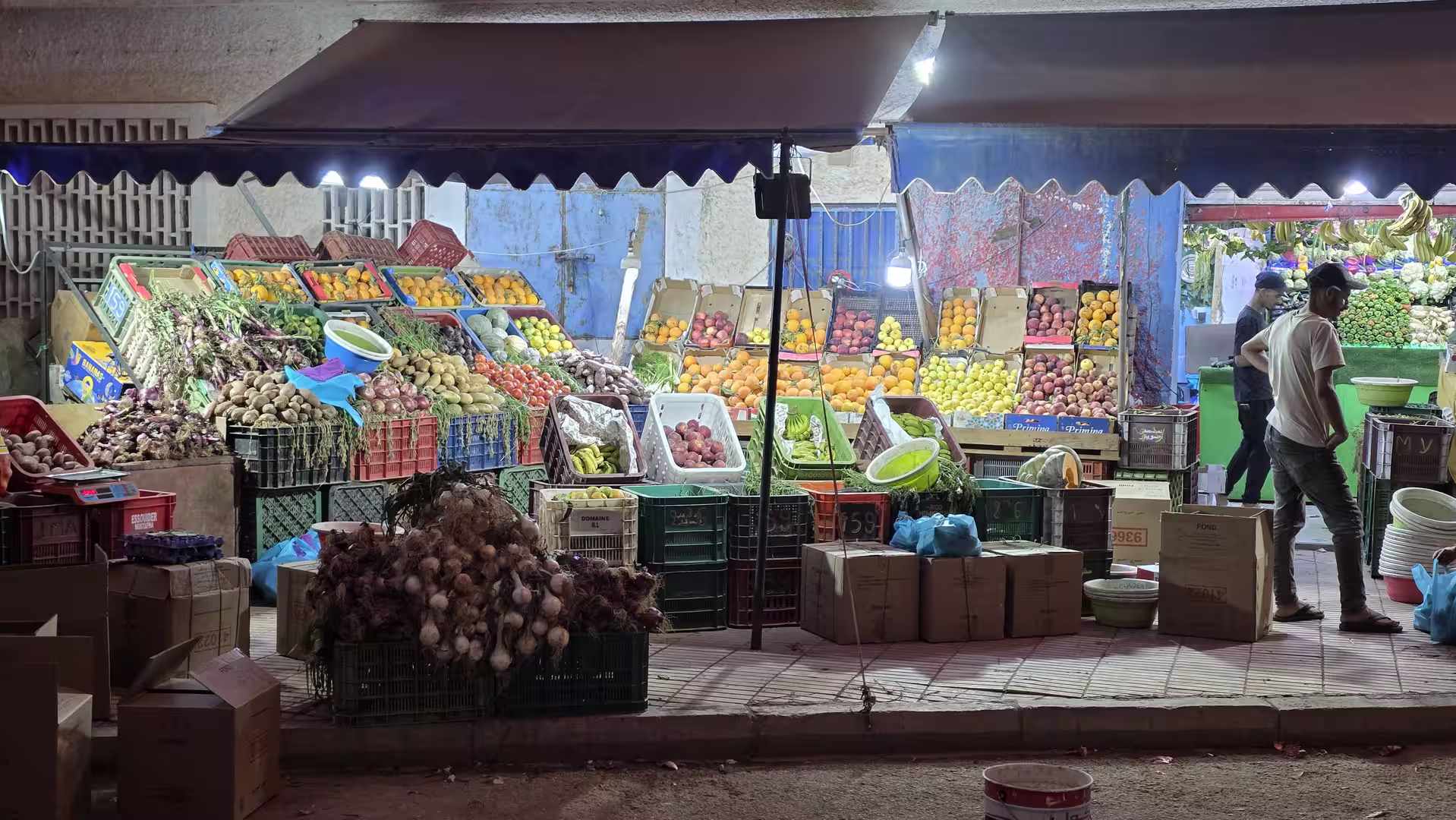 Evening street market with illuminated fruit and vegetable stalls displaying fresh produce in Dakhla.