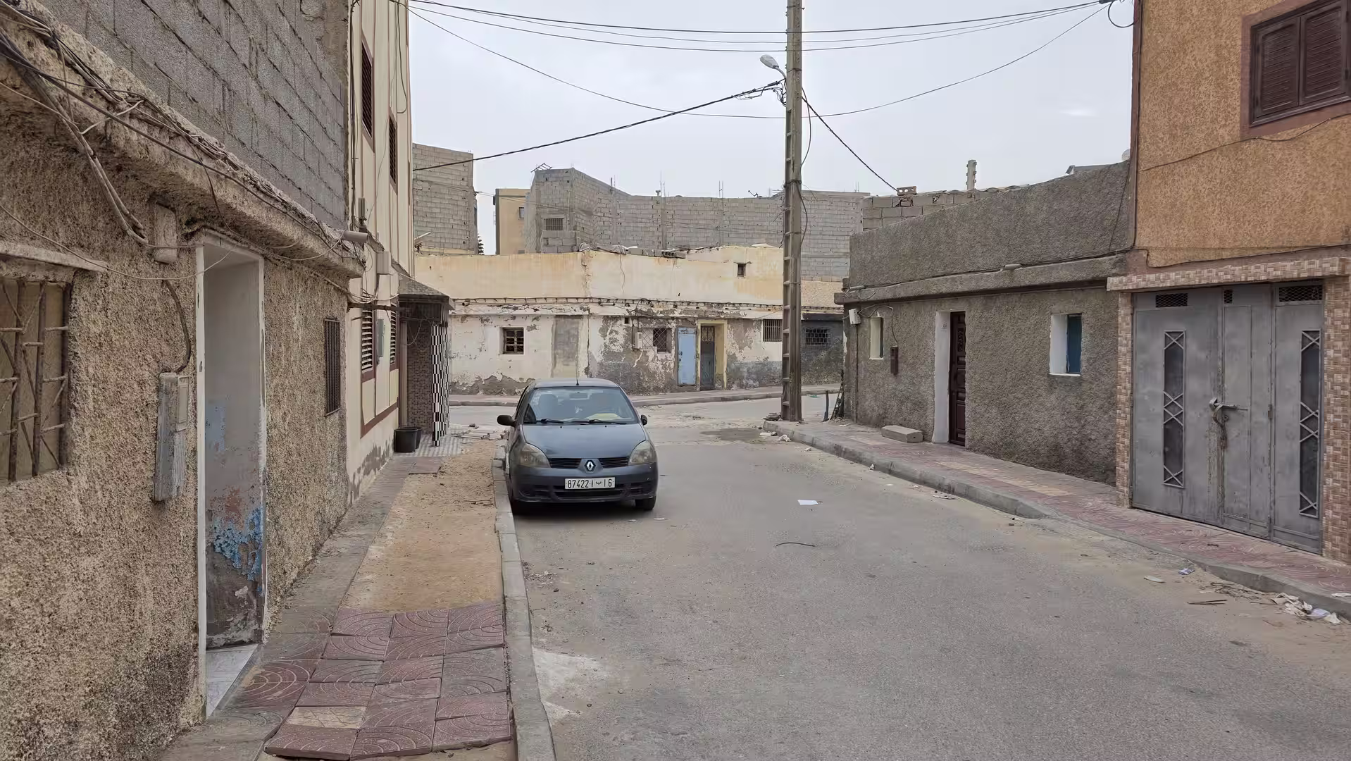 Narrow residential street in Dakhla with simple concrete houses, a parked car and overhead utility lines.