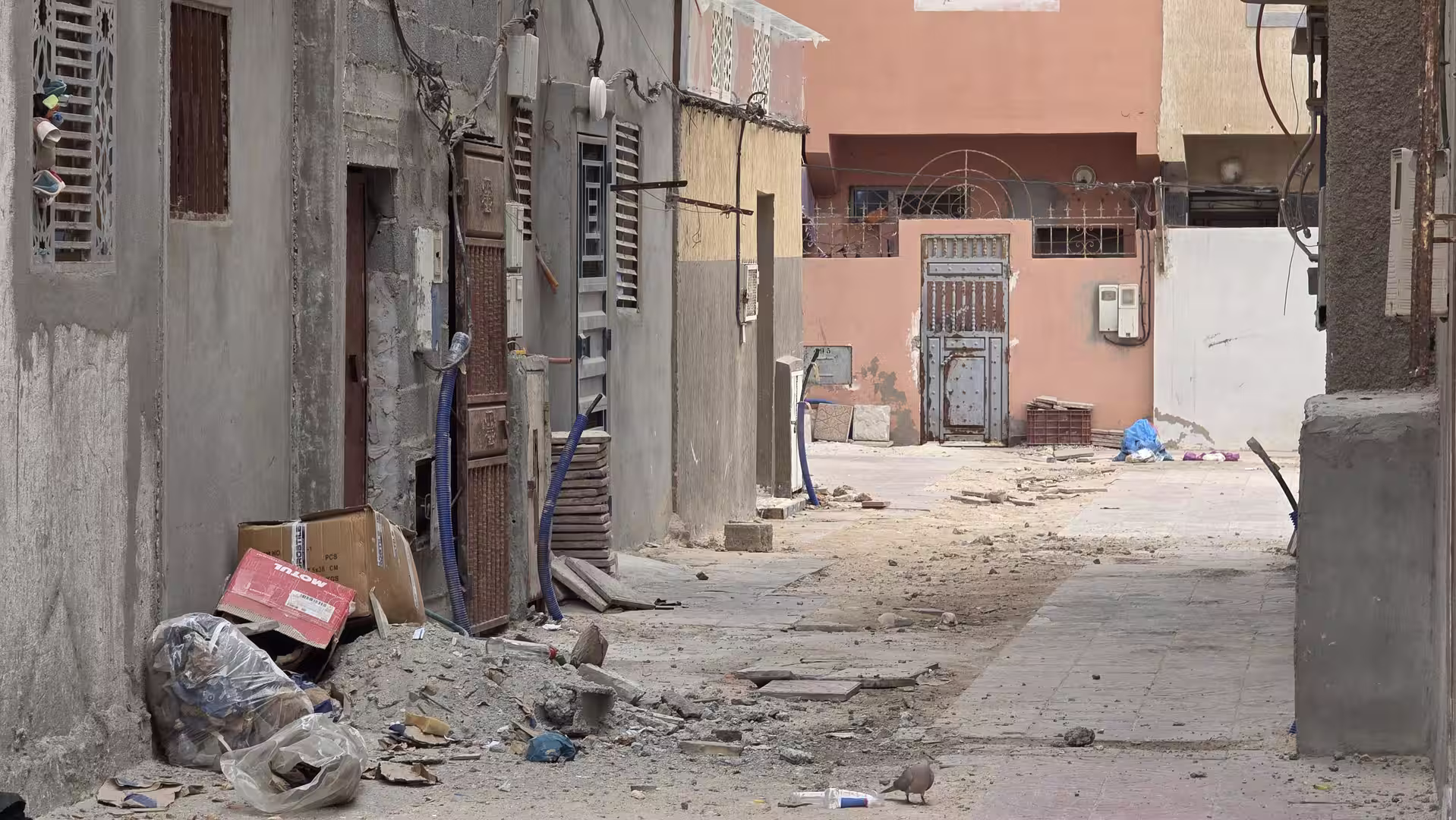 Narrow alley in a residential area of Dakhla with unfinished surfaces, utility cables and scattered construction debris.