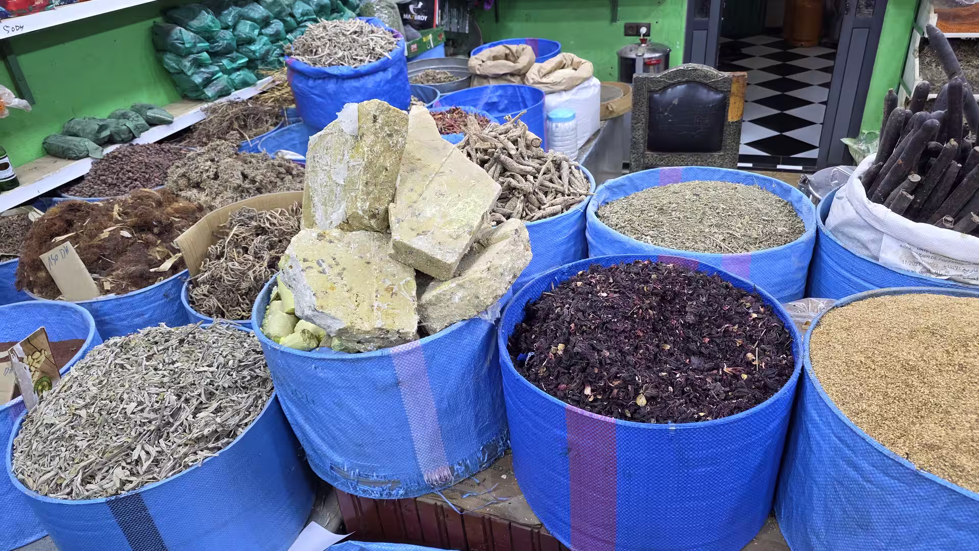 Open sacks filled with dried herbs, seeds, roots and plant products displayed at a traditional market stall.
