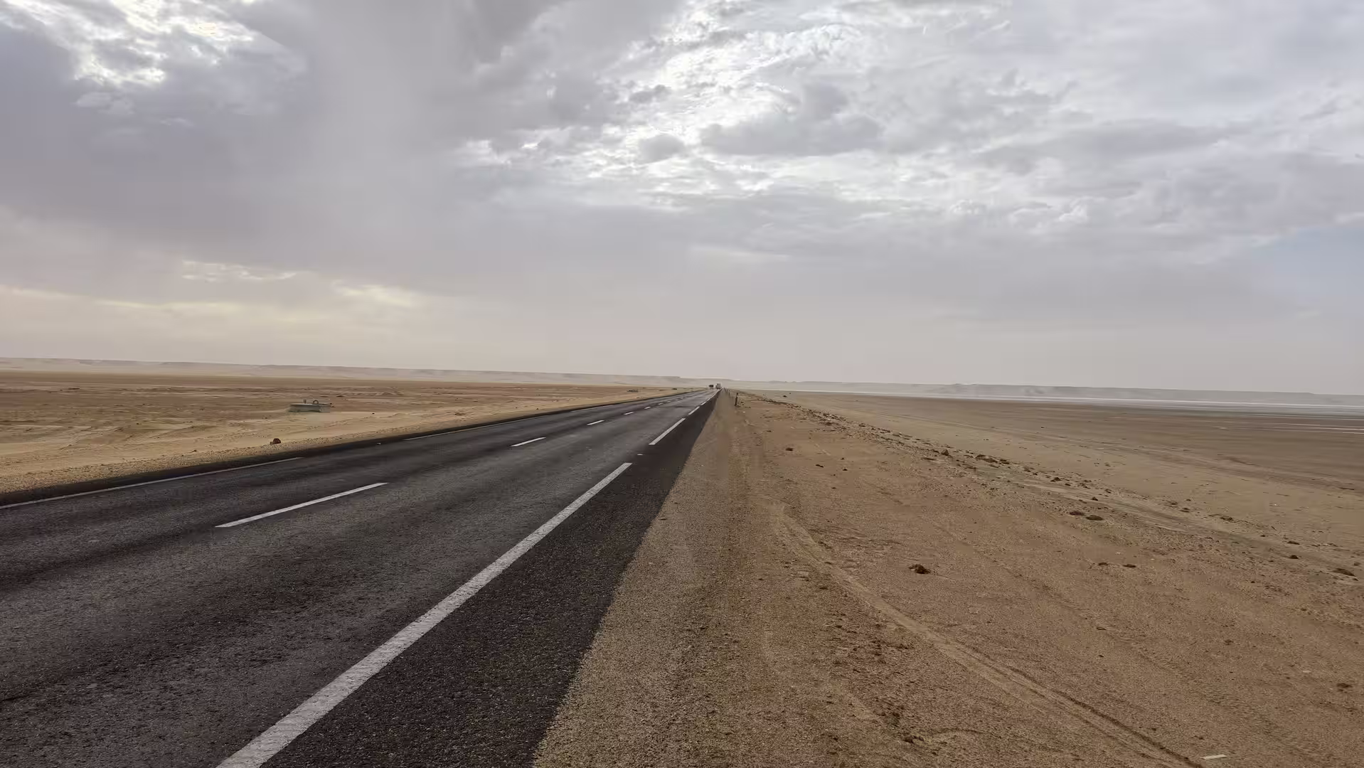 Long straight road crossing the desert landscape south of Dakhla beneath dramatic clouds and open skies.