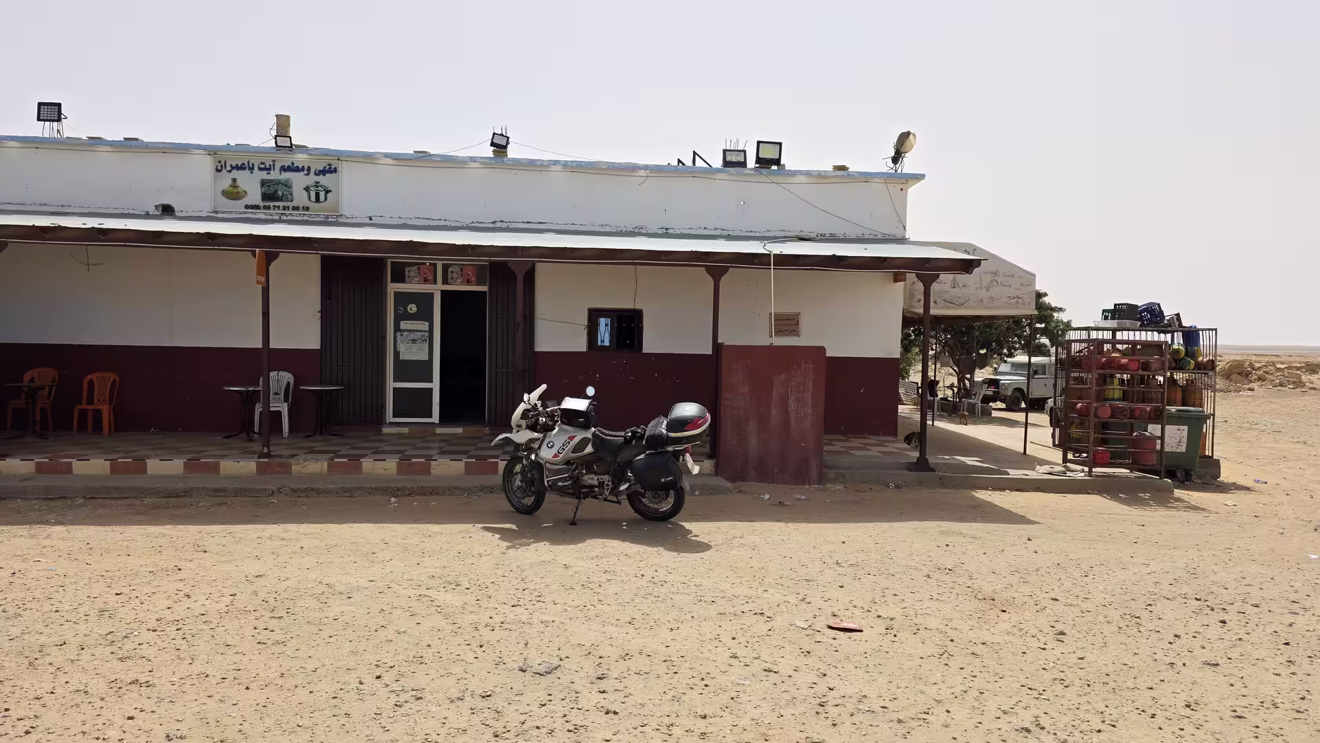 Motorcycle parked in front of a small roadside café and restaurant in the desert during a northbound journey through southern Morocco.