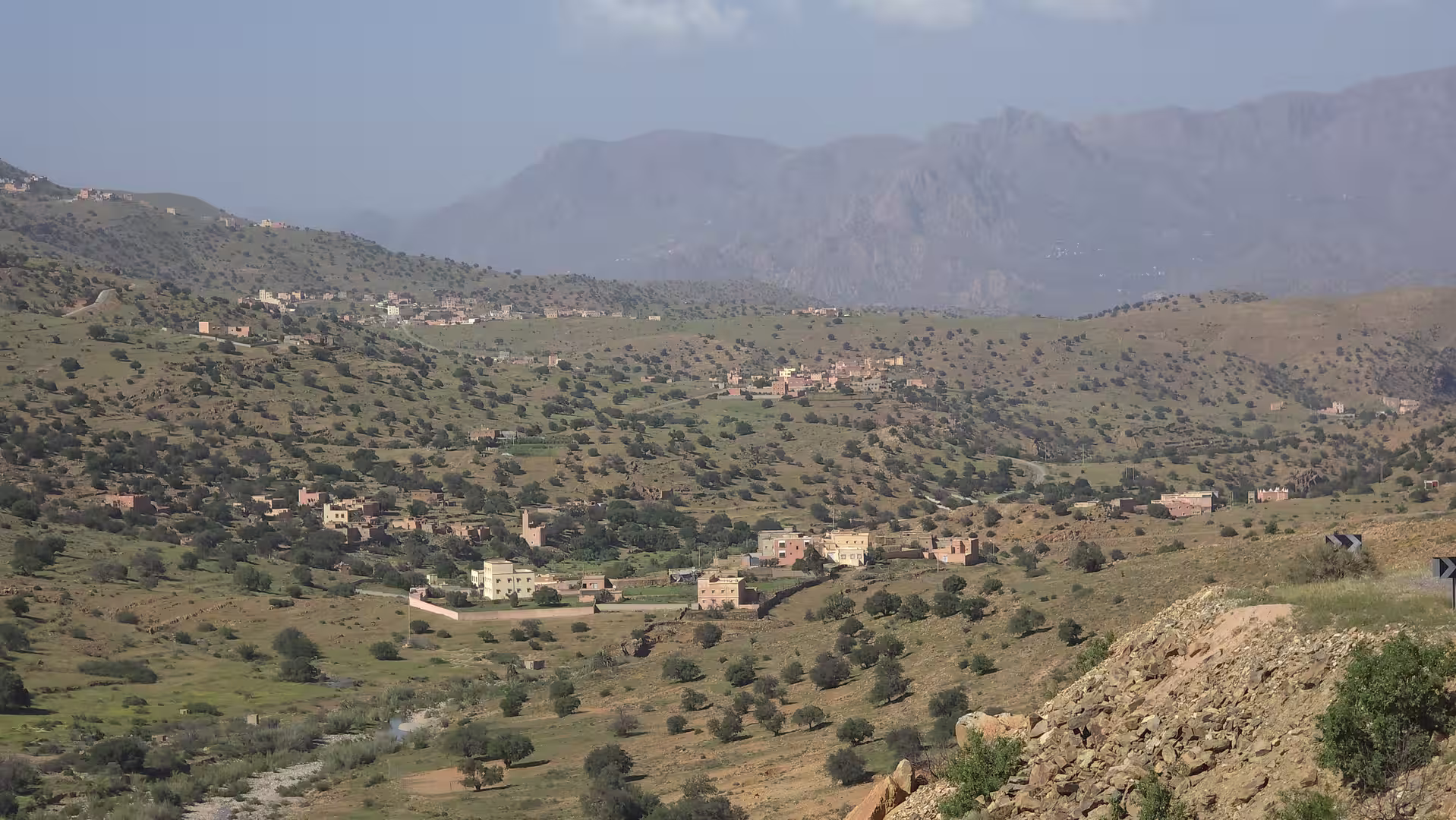 Wide view across a green mountain valley in Morocco with scattered villages, rolling hills and distant mountain peaks.