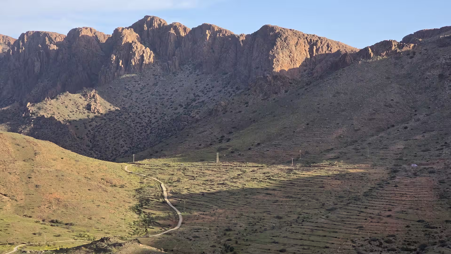 Mountain valley near Tafraoute with a narrow road leading through terraced slopes beneath steep granite cliffs.
