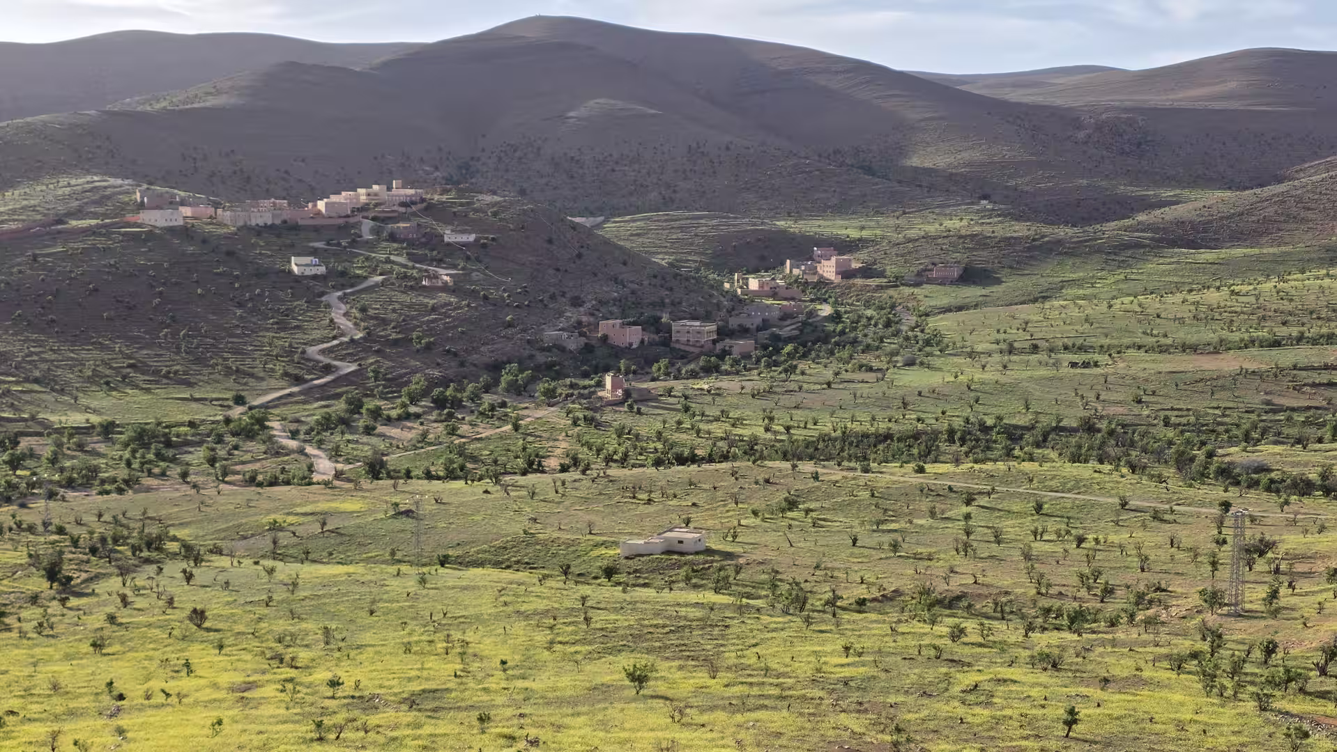 Wide valley landscape near Tafraoute with scattered villages, green fields, and winding roads between rounded mountain hills.