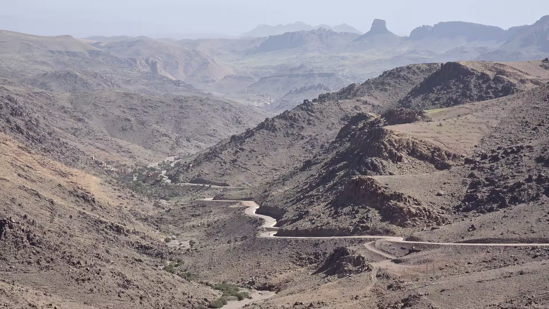 Mountain road winding through a broad rocky valley in the Anti-Atlas with layered peaks in the distance.