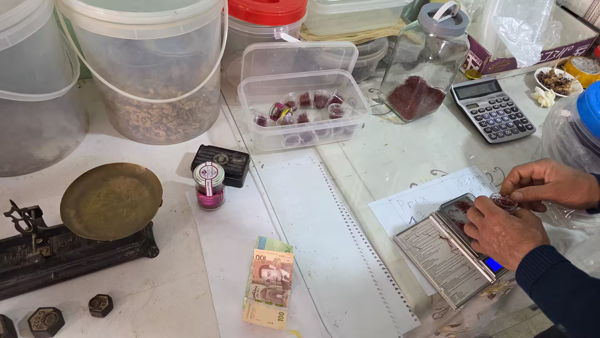 A vendor weighing small portions of saffron on a digital scale at a traditional market counter.
