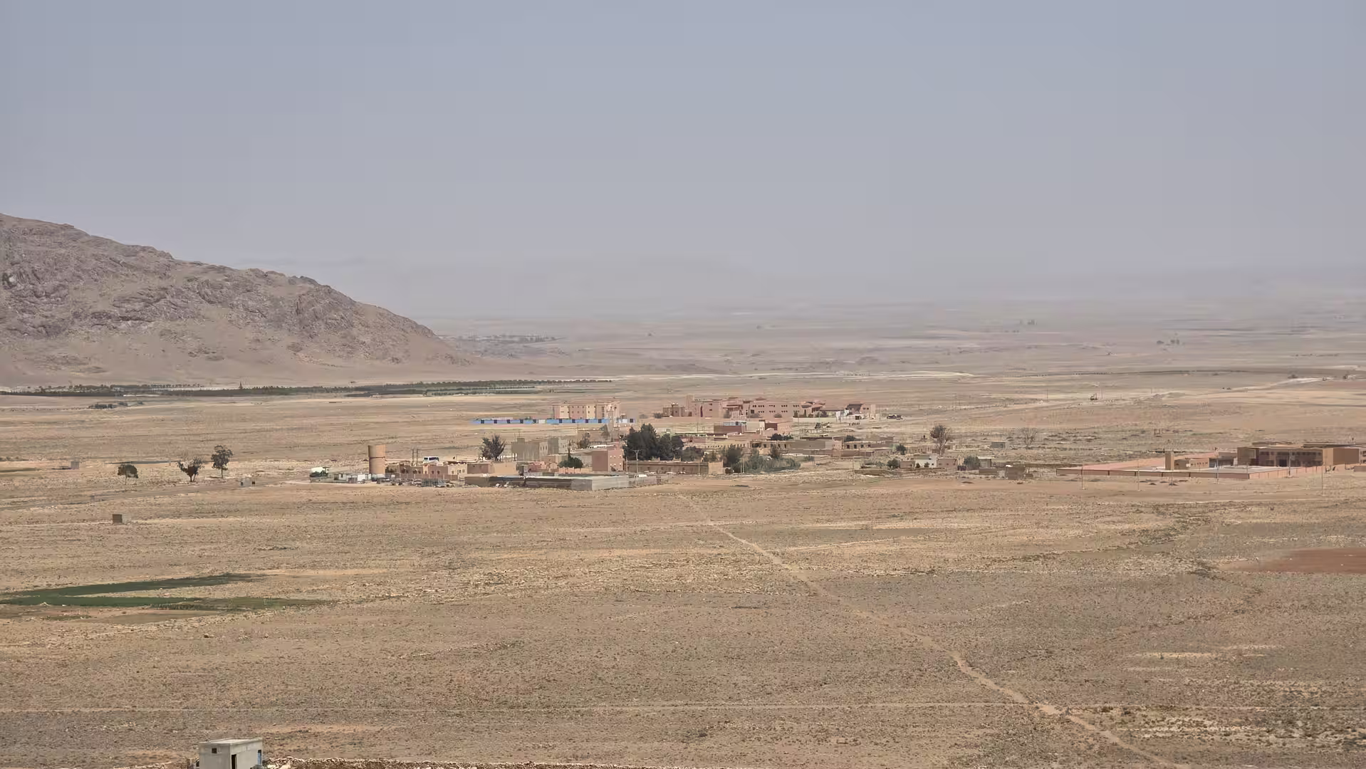 A remote settlement spread across a broad dry plain below a mountain ridge in the Atlas region.