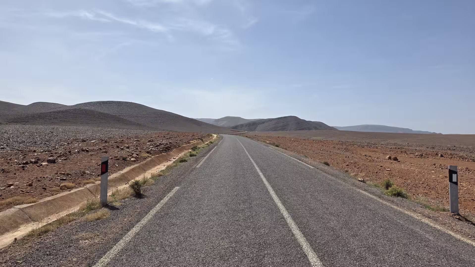 A paved road crossing an open rocky desert plateau toward low mountains in the Atlas region.