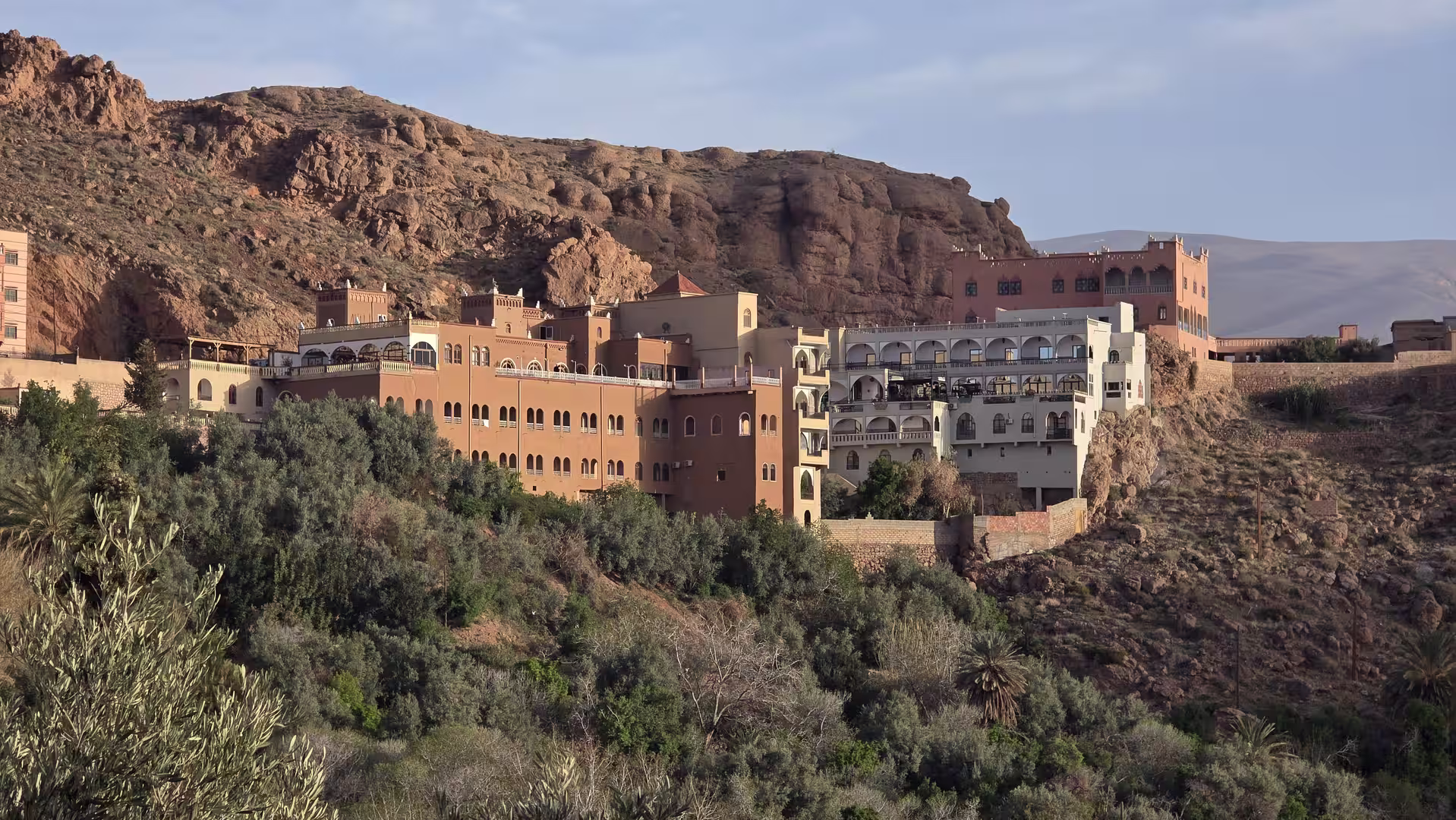Large terraced hotel and hillside buildings overlooking the green oasis of the Dades Valley shortly after sunrise near Boumalne, Morocco.