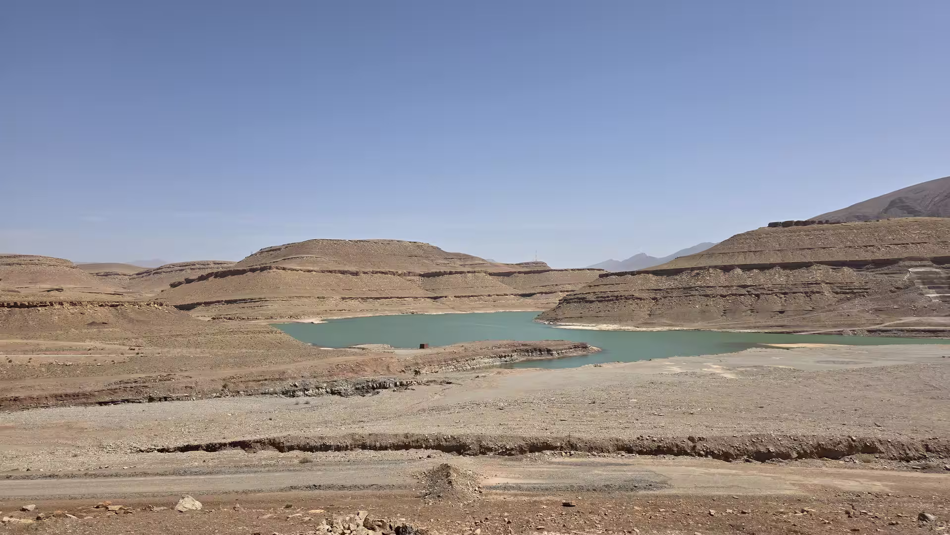 Turquoise reservoir surrounded by dry terraced hills and exposed shoreline within an arid mountain landscape of the Atlas region.
