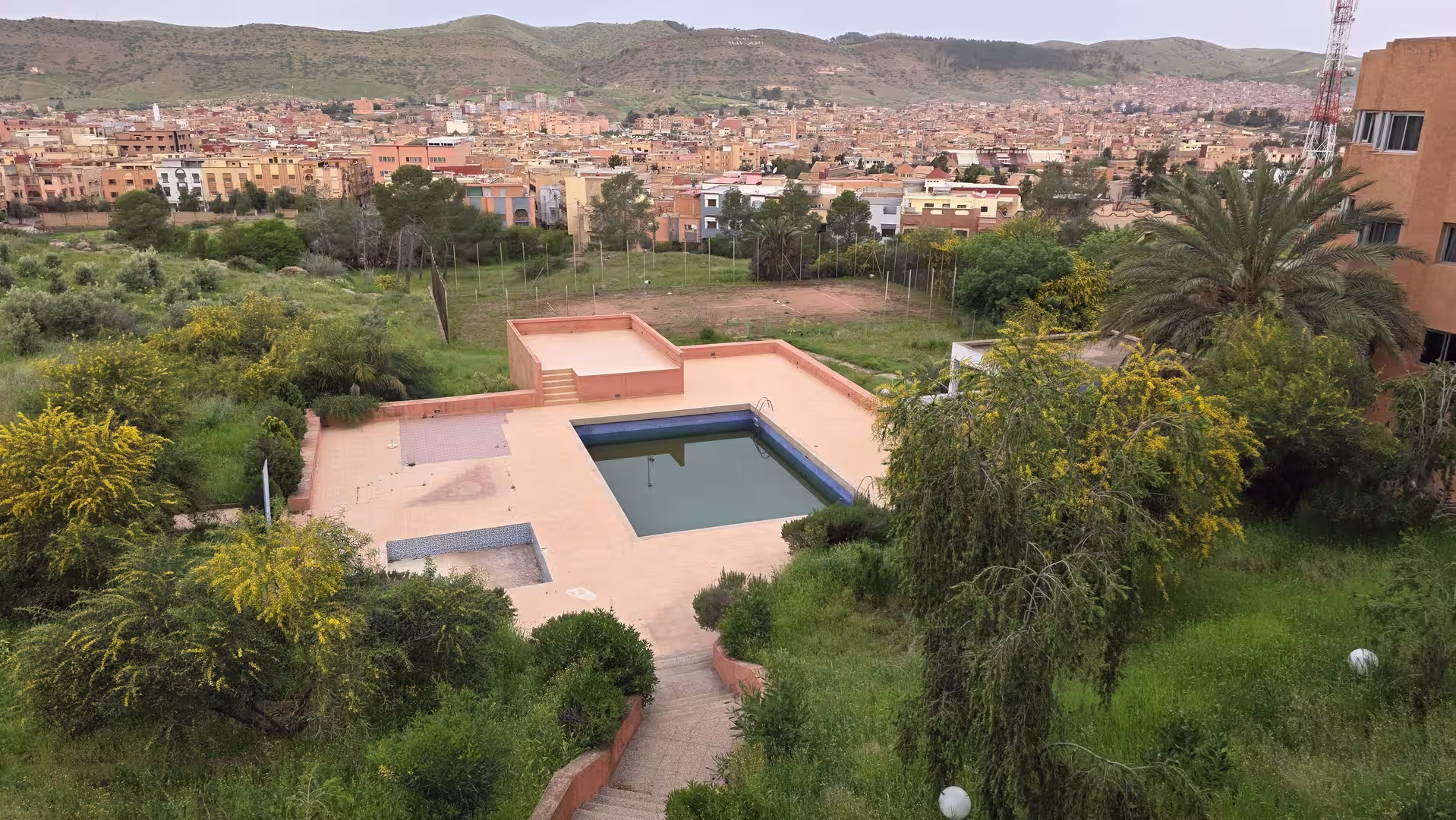 View from Hotel Continental in Khénifra overlooking the hotel pool area, surrounded by greenery, with the city and hills in the background.