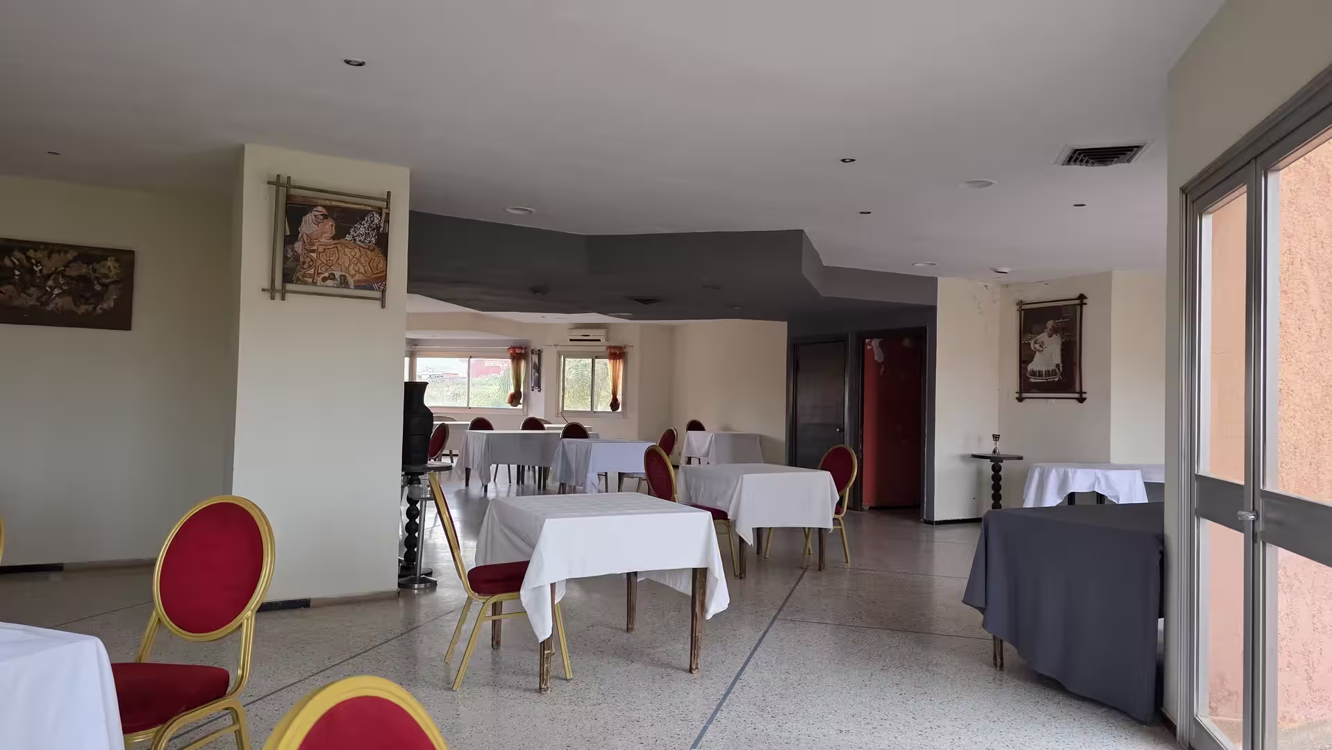 Dining area at Hotel Continental in Khénifra with neatly arranged tables, red chairs, and natural light entering through large windows.