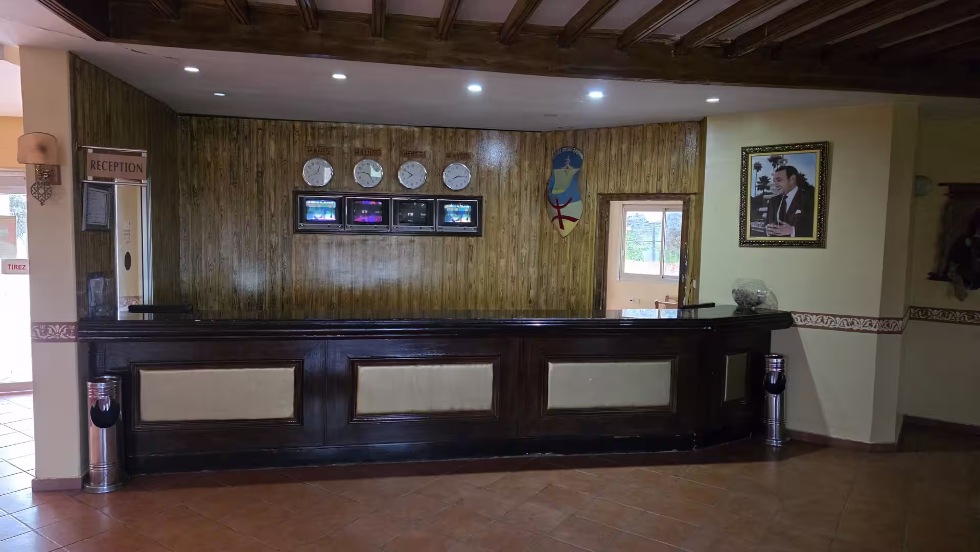 Reception area at Hotel Continental in Khénifra featuring a dark wood front desk, world clocks, and a classic hotel lobby design.