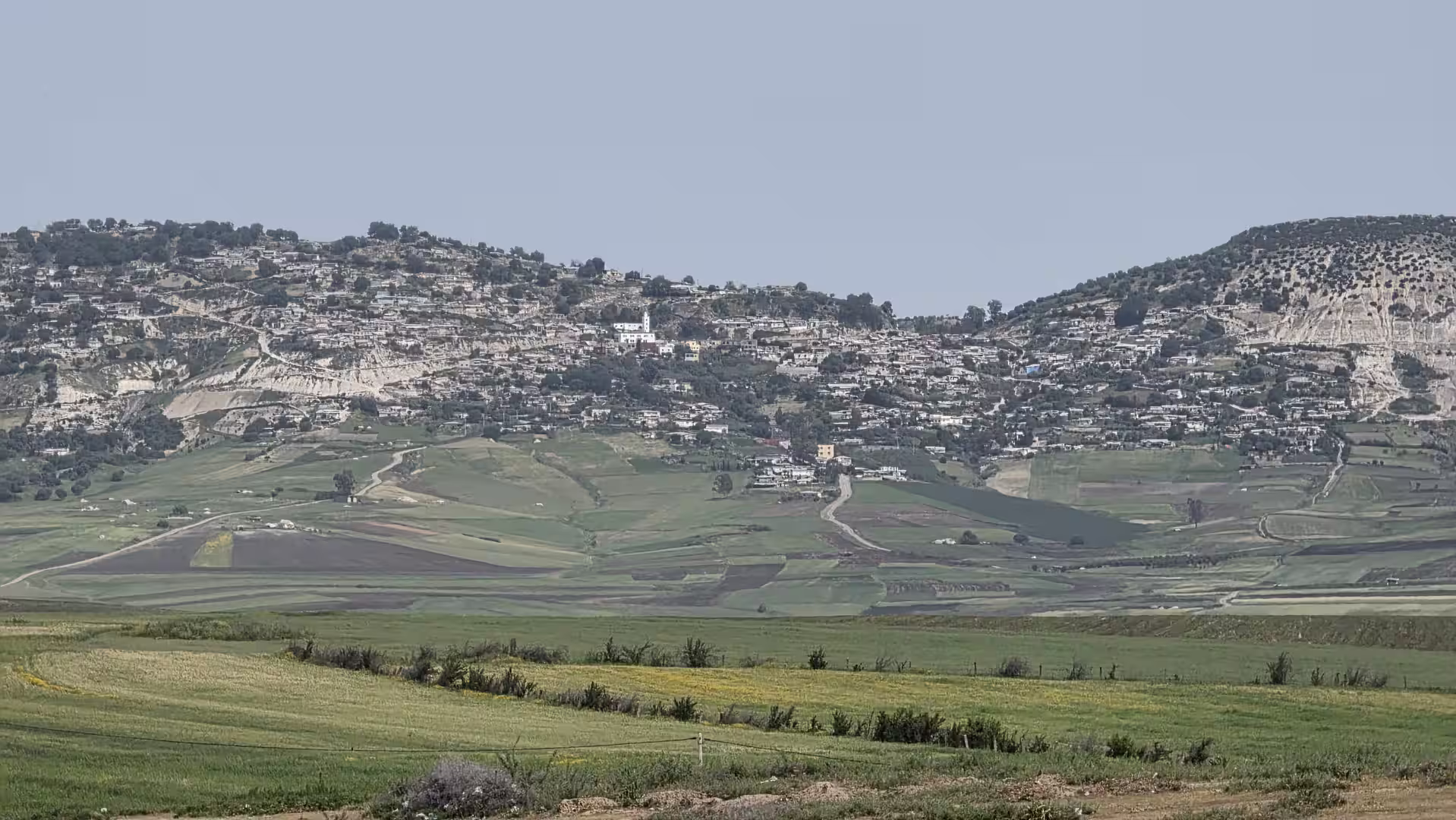 Panoramic view of green agricultural fields and a hillside village along the route between Khénifra and Tanger Med in northern Morocco.