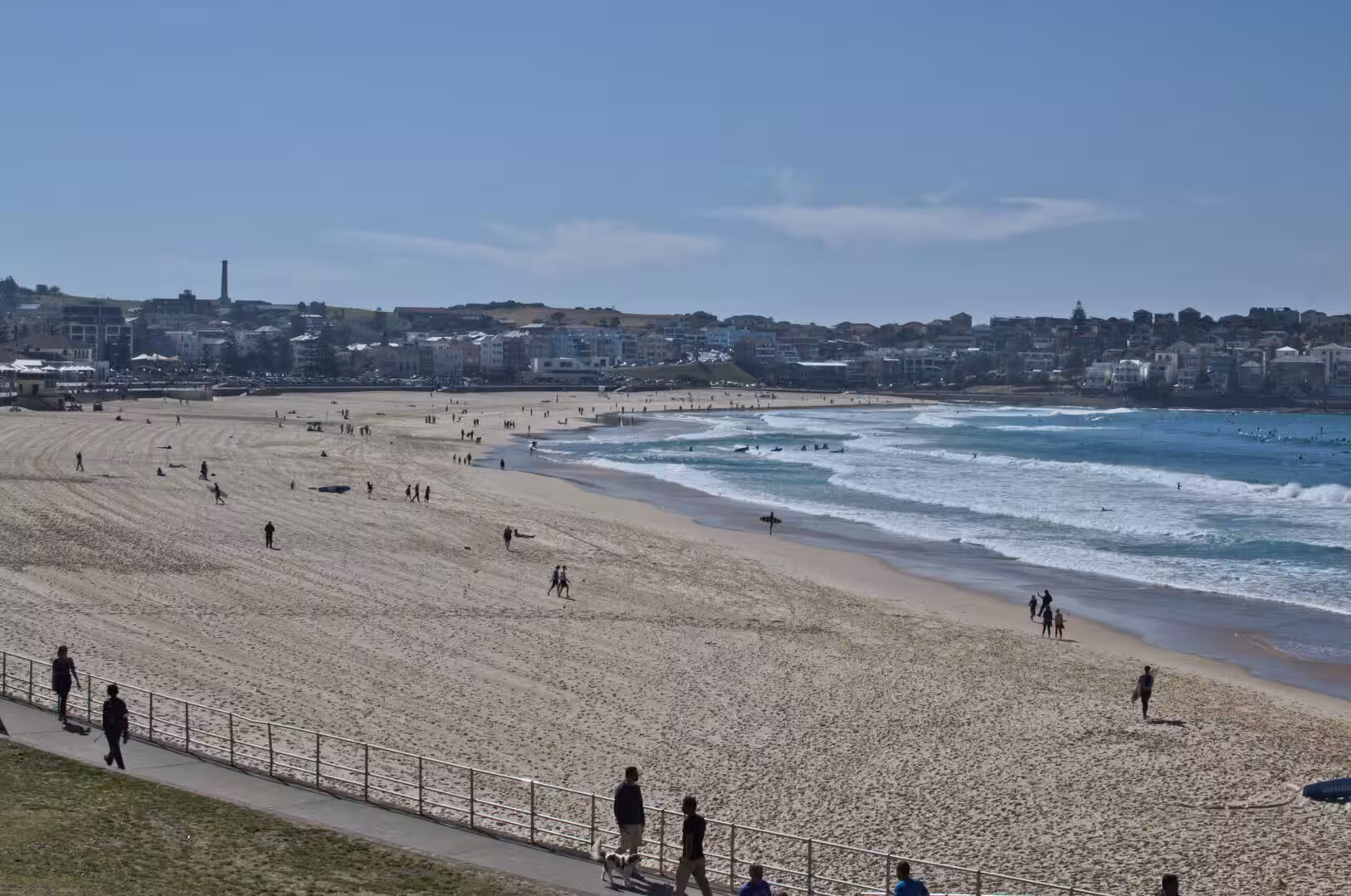 A sprawling sandy beach curves beside turquoise surf toward a low suburb skyline.