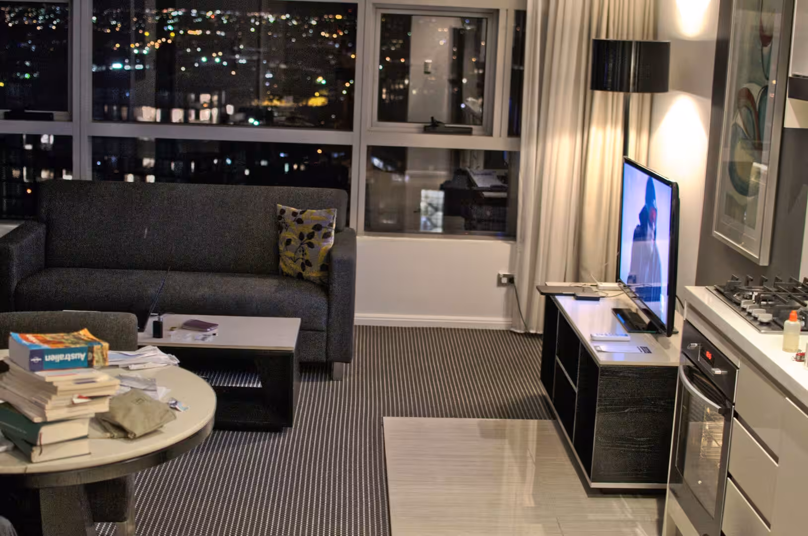 A dim apartment lounge with a grey sofa and glowing city lights through the window.