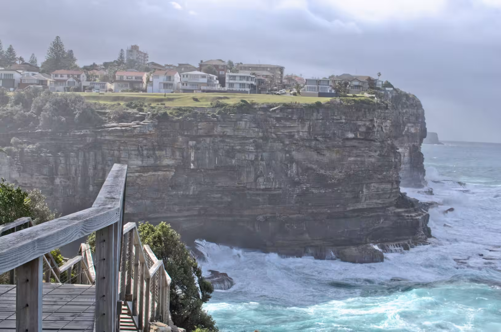 Timber stairs wind down beside a towering, wave-battered cliff face.