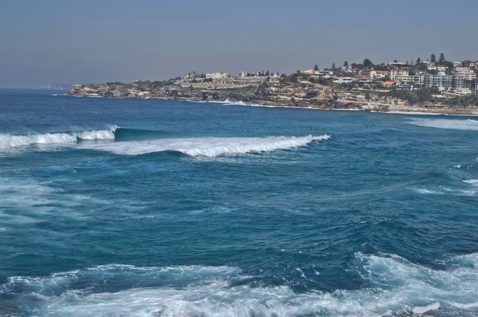 Surfers sit in the lineup as big swell rolls toward the headland.