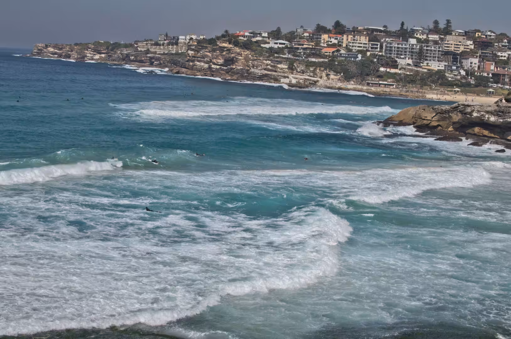 Lines of surf swell toward the beach beneath the clifftop homes.