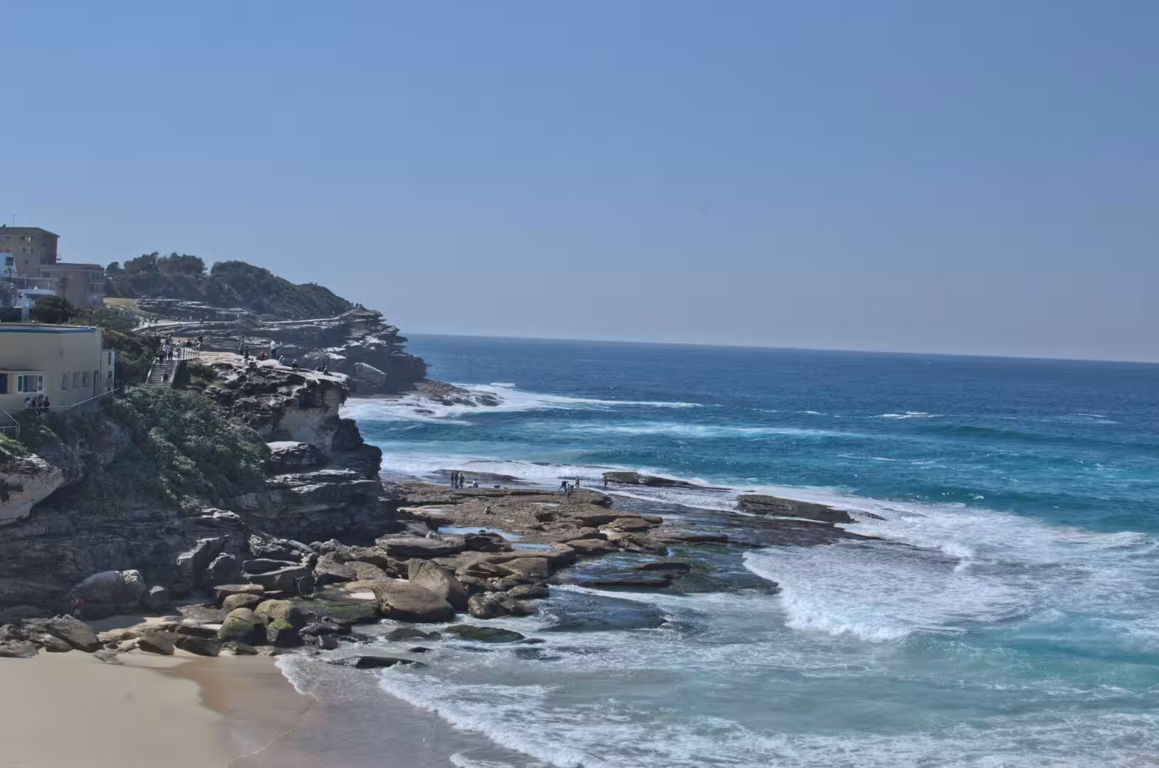 White surf crashes against the rocks of a curved coastal headland.