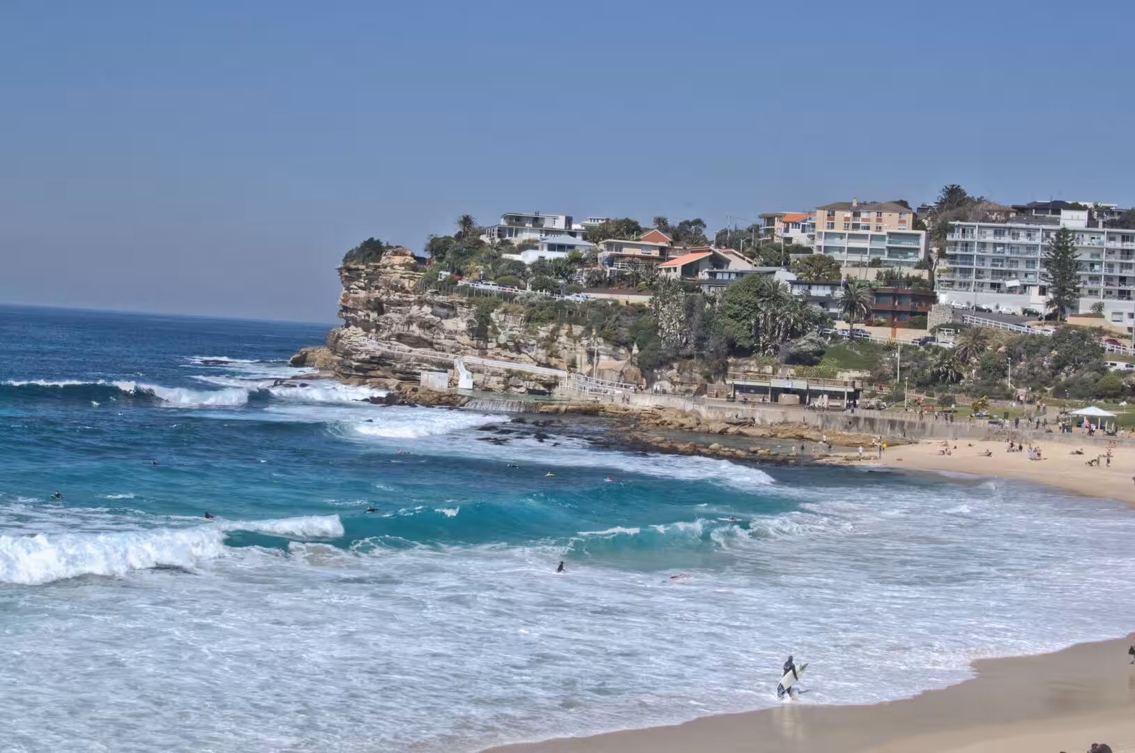 Swimmers dot the surf in a sheltered bay below a cliff-top suburb.