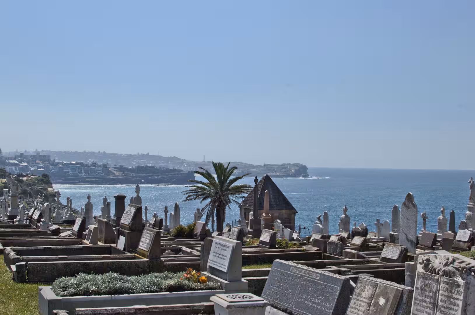 Headstones and a chapel stand on a green cliff above the ocean.