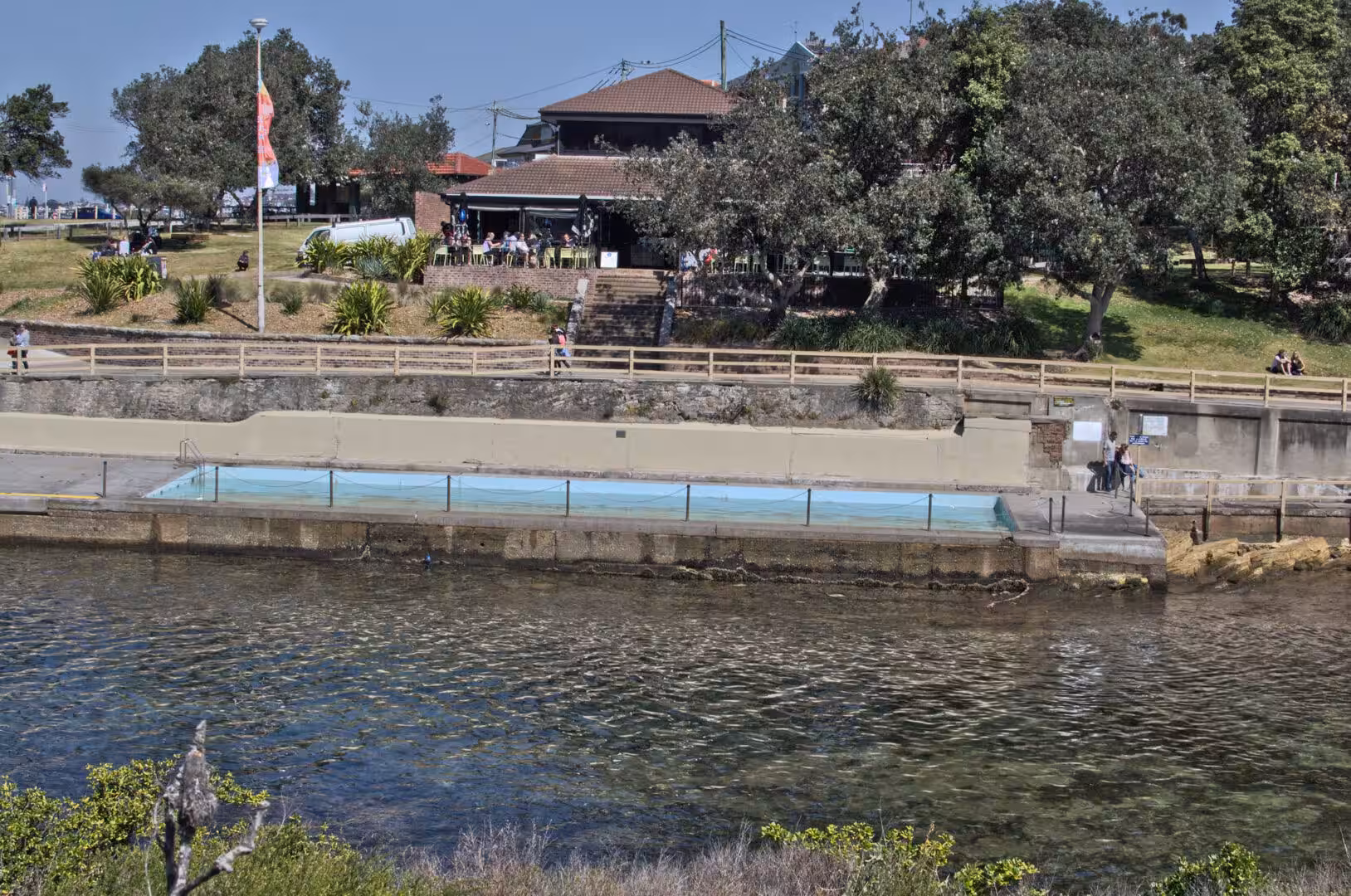 A fenced seawater pool sits beneath a park and cafe deck.