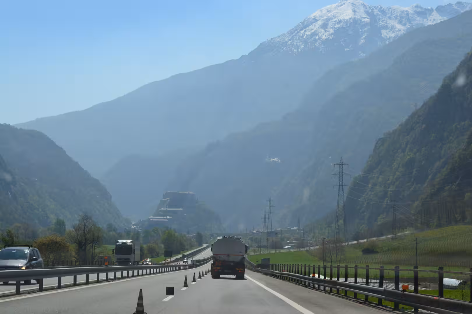 A motorway winds past a snowcapped mountain through a misty green valley.