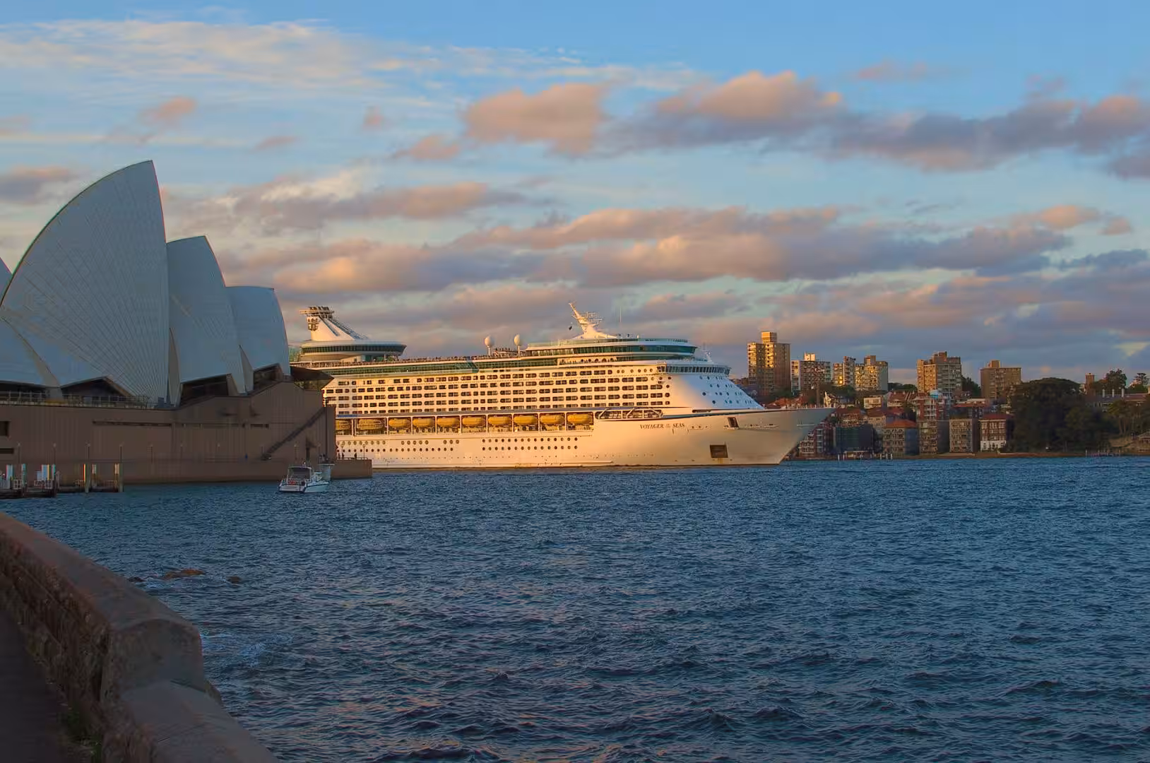 The Opera House's white sails frame a giant cruise ship on the harbour at dusk.