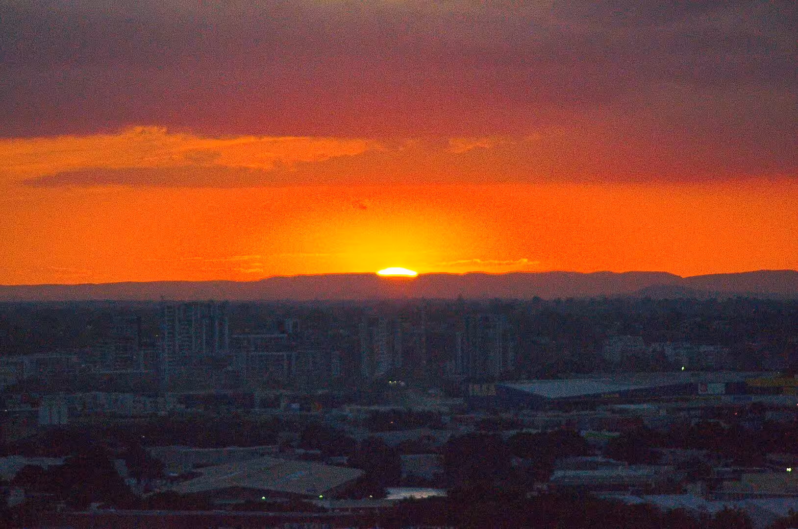 The sun dips behind a ridge, flooding the sky orange over a dark city.