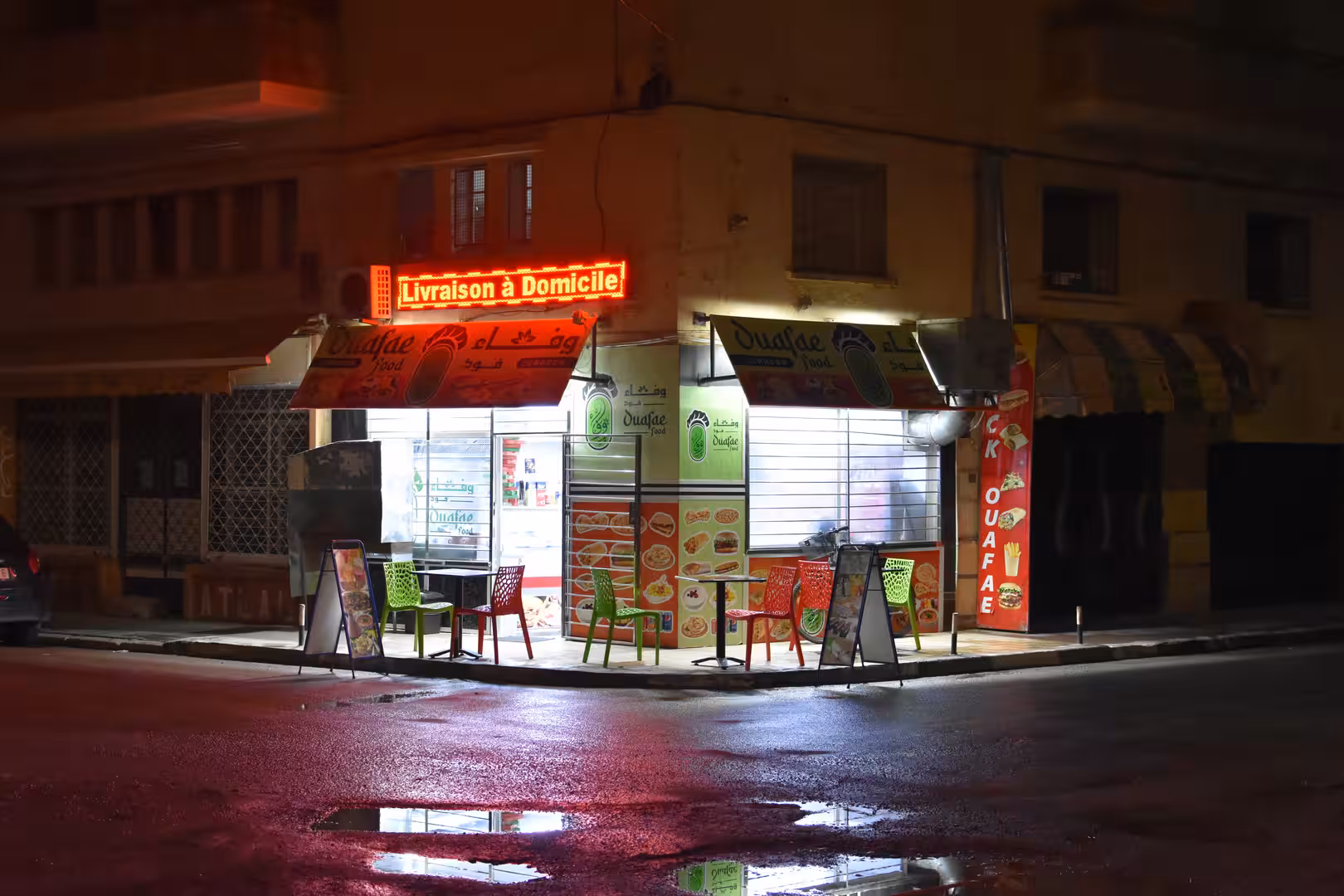 Illuminated takeaway restaurant on a street corner in Oujda at night.