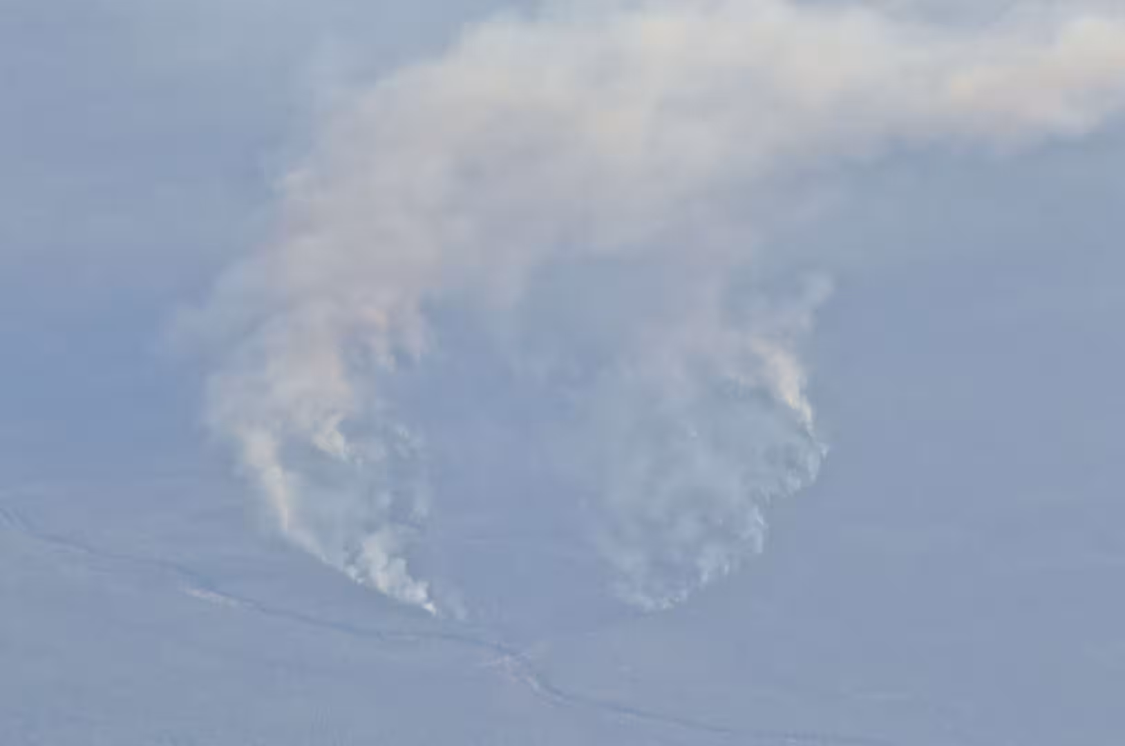 A fluffy white cloud drifts above a hazy, pale expanse of water along the horizon.