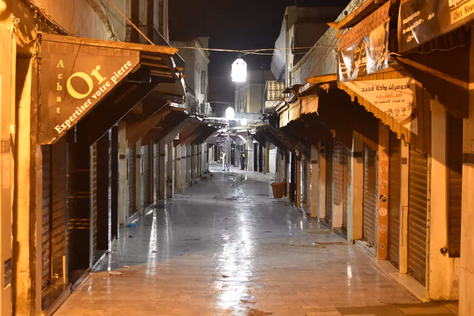 Narrow market street with closed shops illuminated by lanterns in Oujda after dark.