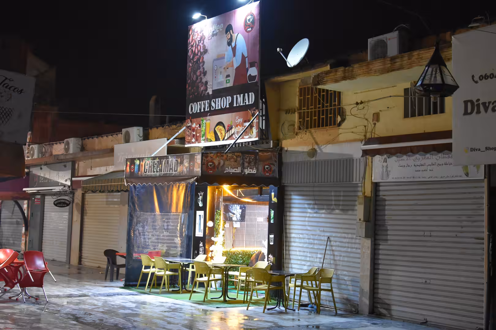 Small coffee shop with outdoor seating illuminated at night in Oujda.