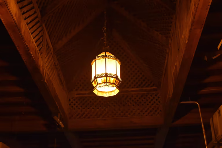 A handcrafted lantern casting warm light beneath traditional Moroccan woodwork.
