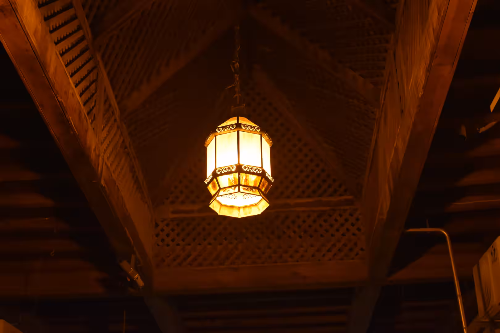Decorative Moroccan lantern hanging beneath a carved wooden ceiling.