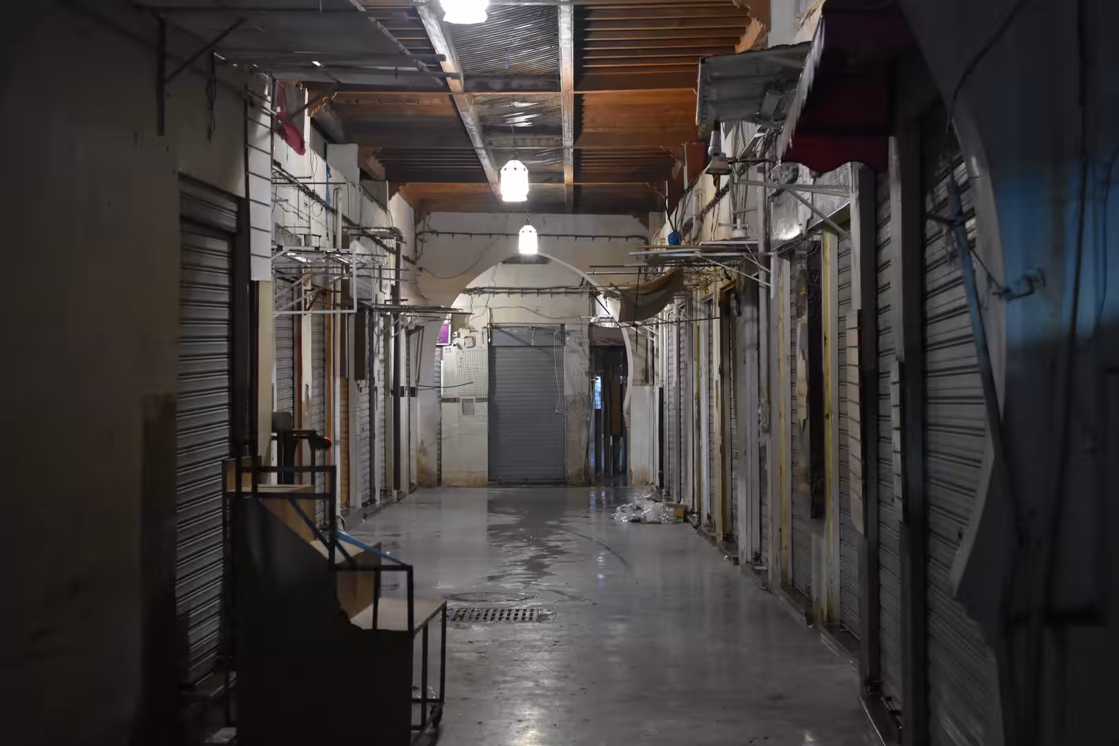 Covered market corridor with closed shops and hanging lights during the evening.